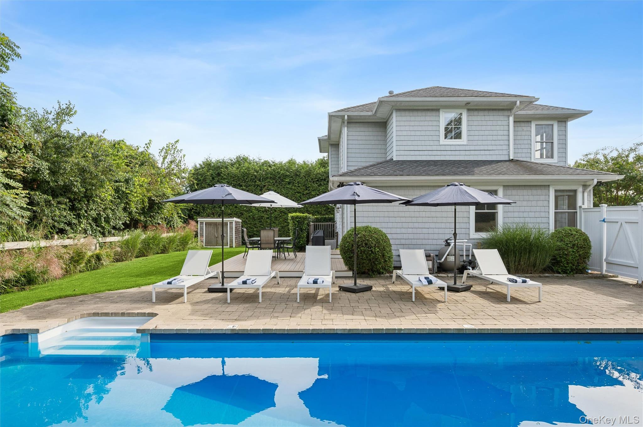 Swimming pool and patio with lounge chairs and umbrellas beside a gray two-story home.