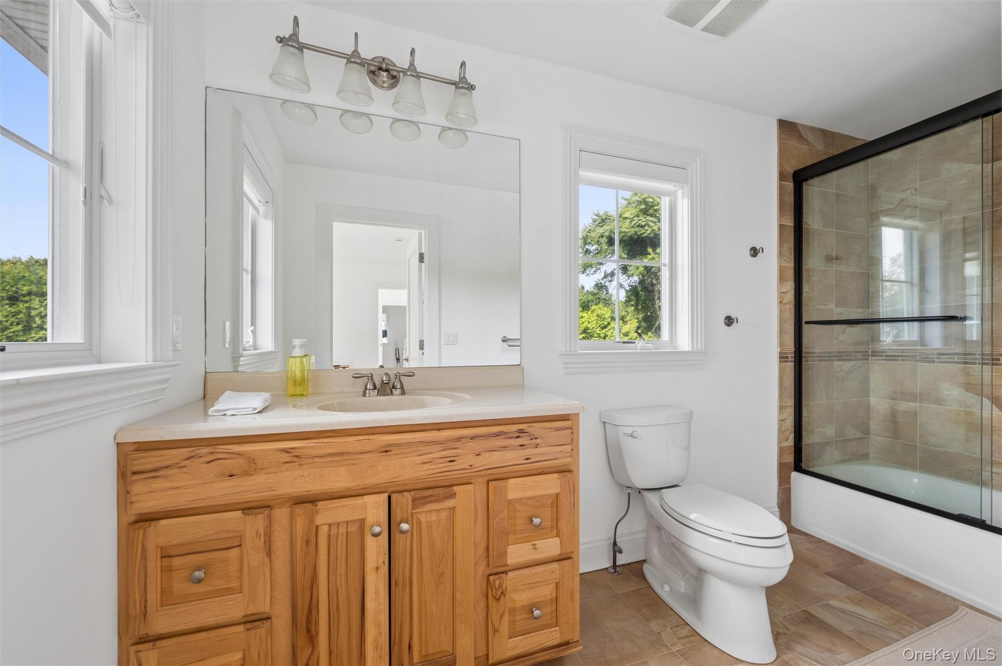 Bright bathroom with a natural wood vanity and a glass-enclosed, tan-tiled shower.