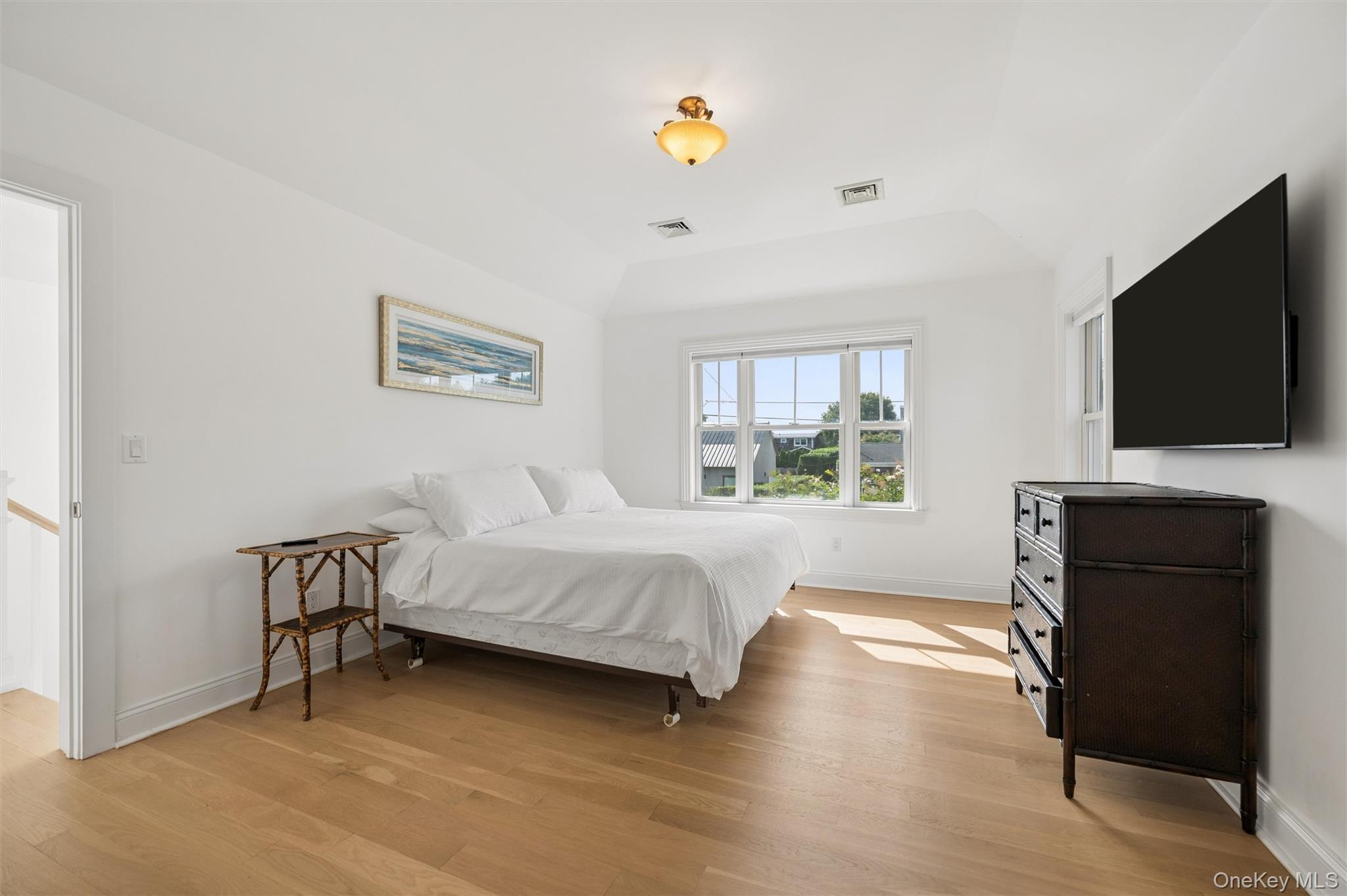 Bright bedroom with a white bed, hardwood floors, and a large window.