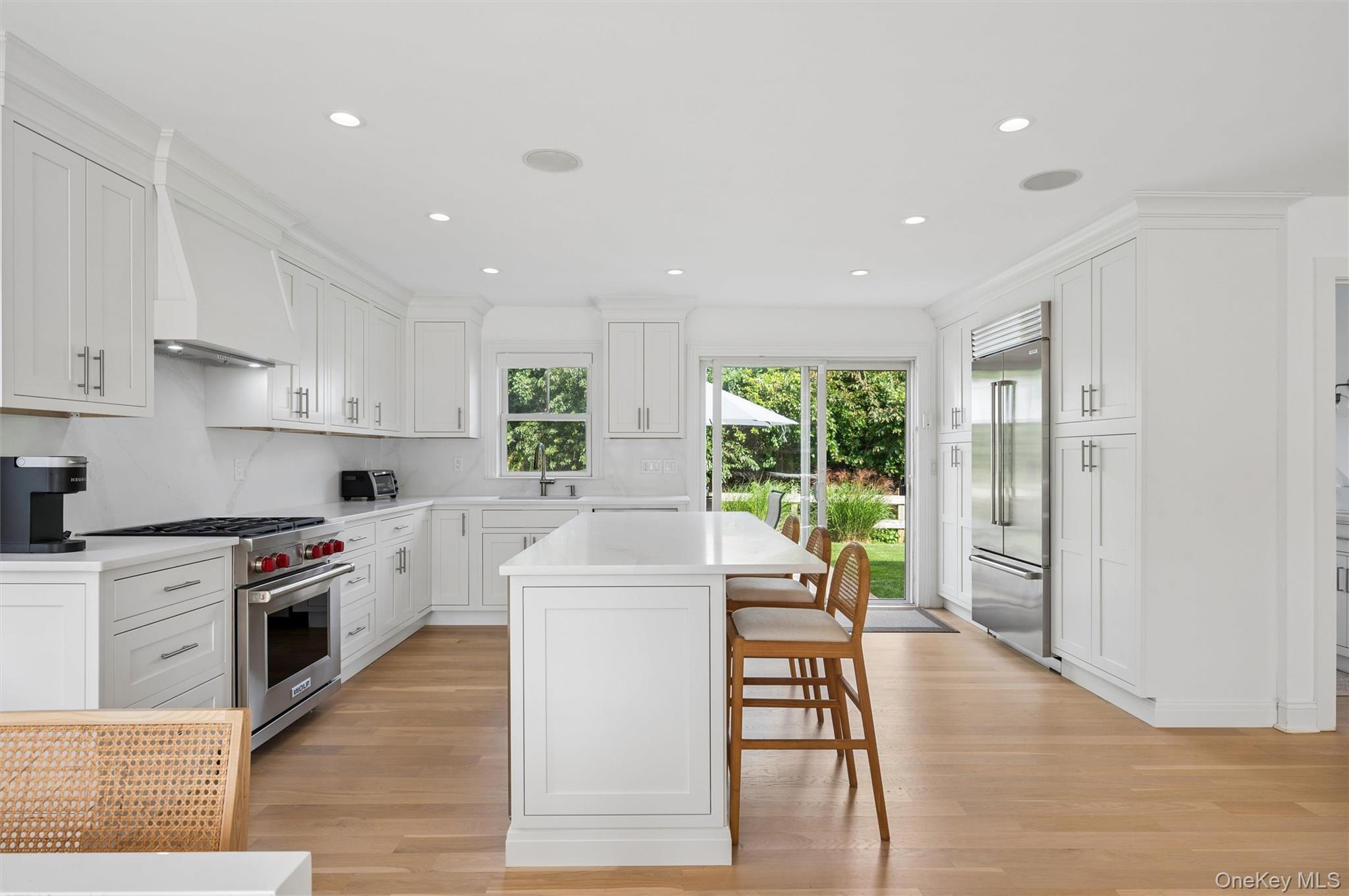 Bright white kitchen with a large island, wooden stools, stainless appliances, and sliding doors to the garden.