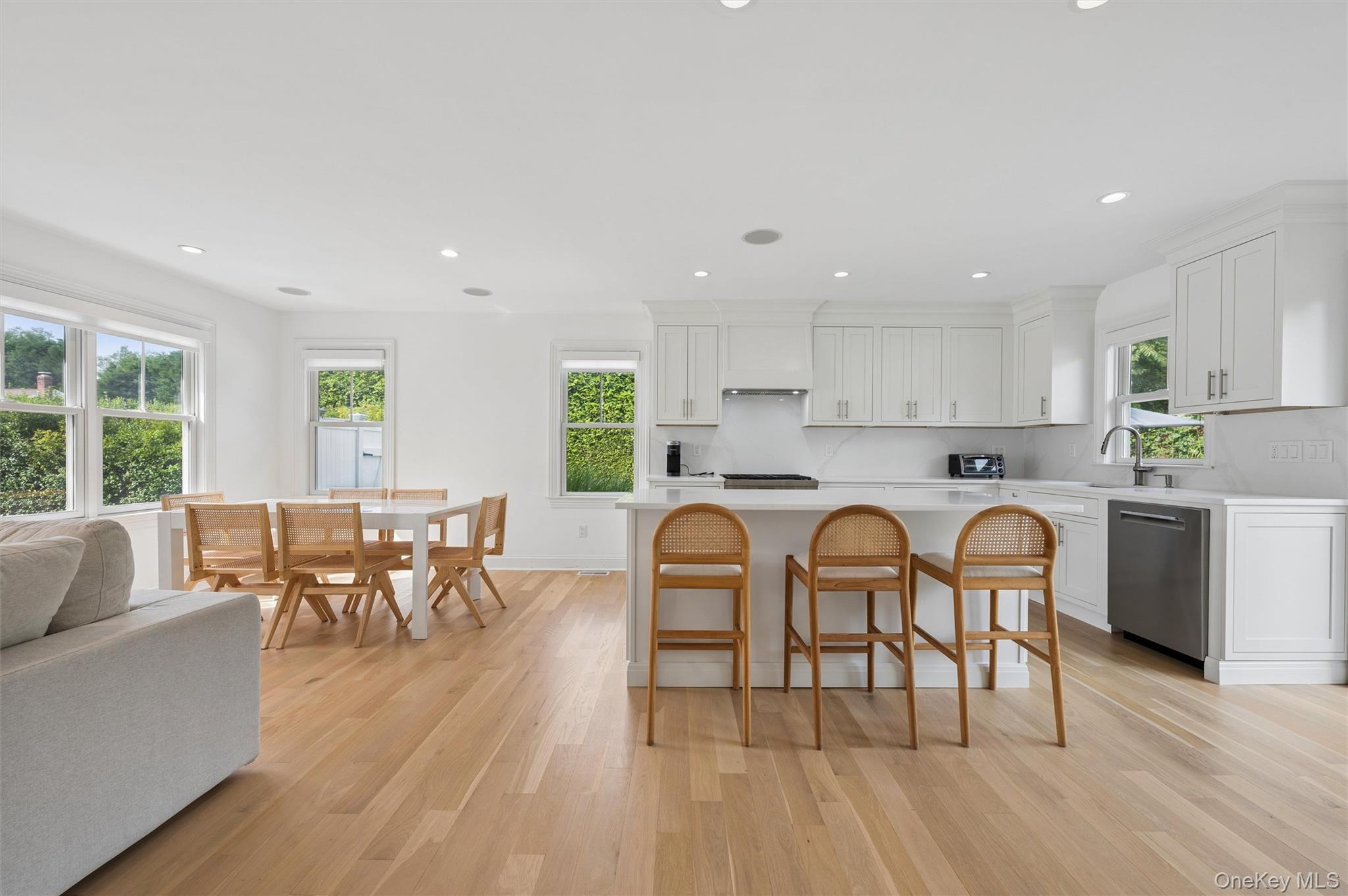 Open-plan kitchen with white cabinetry, an island with three wooden stools, and a dining table by large windows.