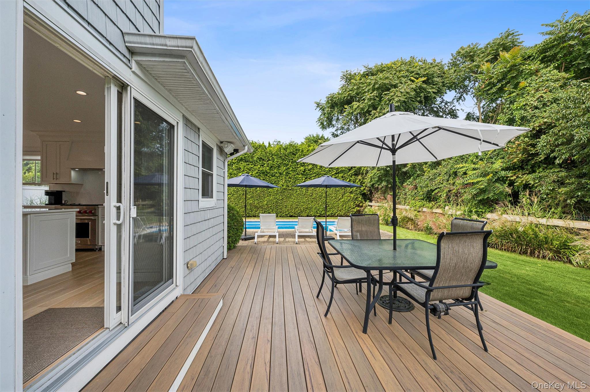 Wood deck with outdoor dining set and umbrella beside a swimming pool.