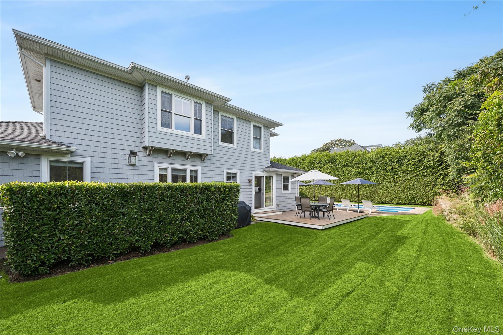Gray two-story home with a deck, swimming pool, and broad green lawn.