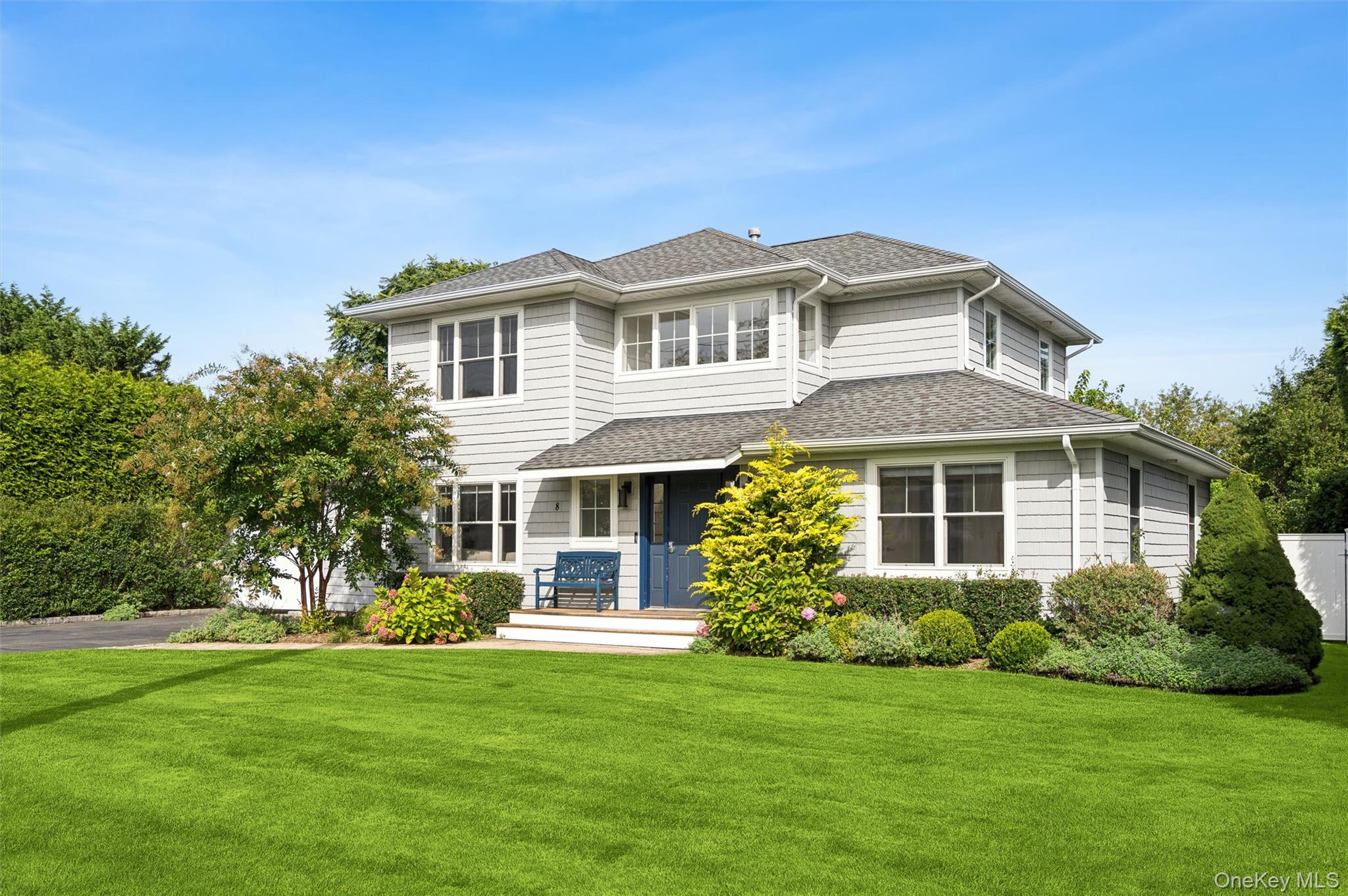 Two-story gray house with a blue front door, landscaped shrubs, and a broad green lawn.