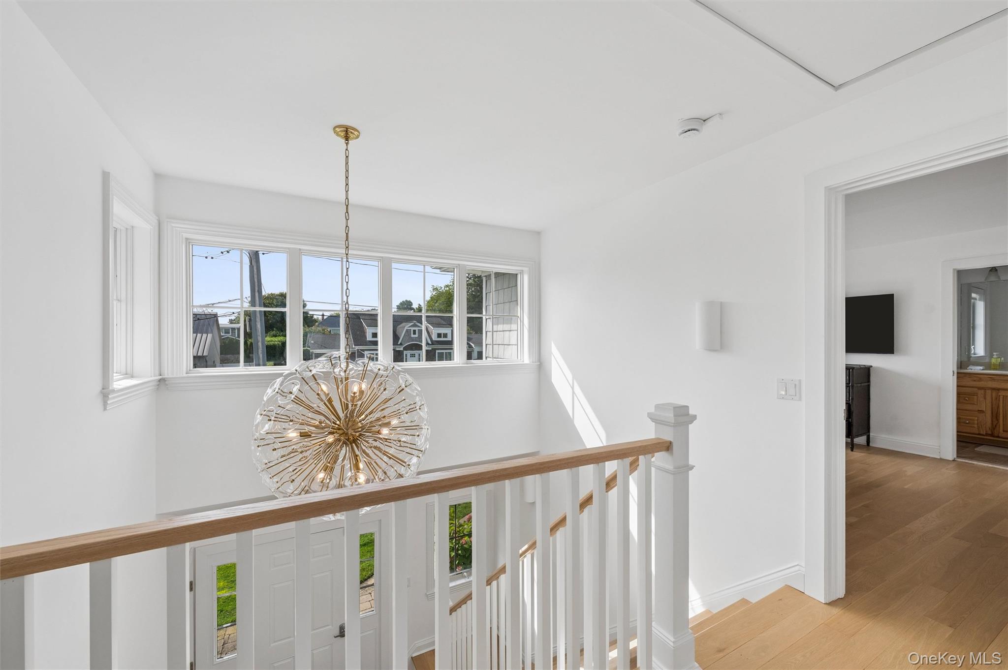 Bright stair landing with a spherical brass chandelier, large windows, and a wooden handrail.