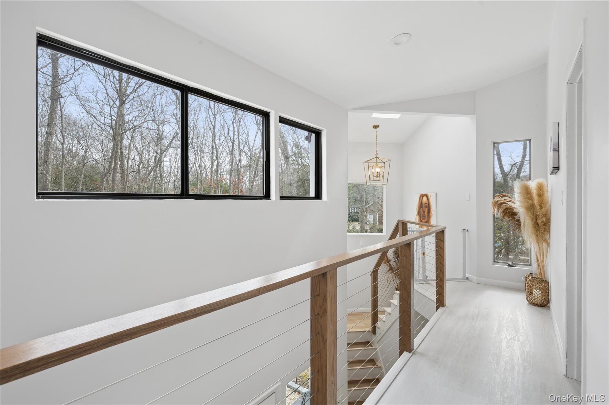 Bright upstairs landing with a wood-and-cable railing and large windows overlooking leafless trees.