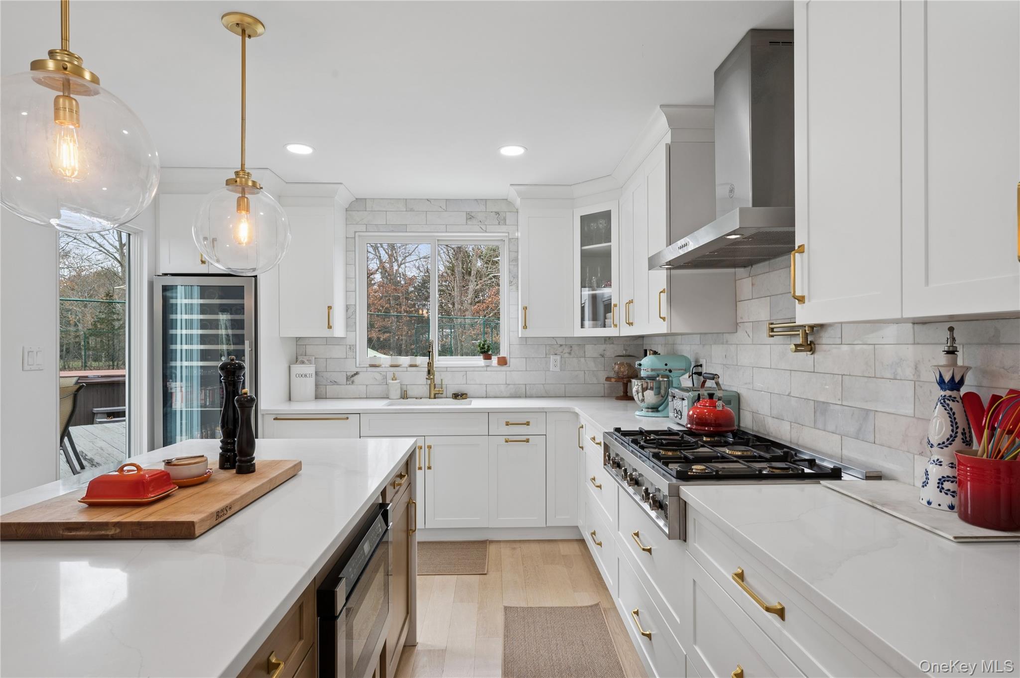 Bright white kitchen with marble tile backsplash, brass fixtures, large island, and stainless steel range.