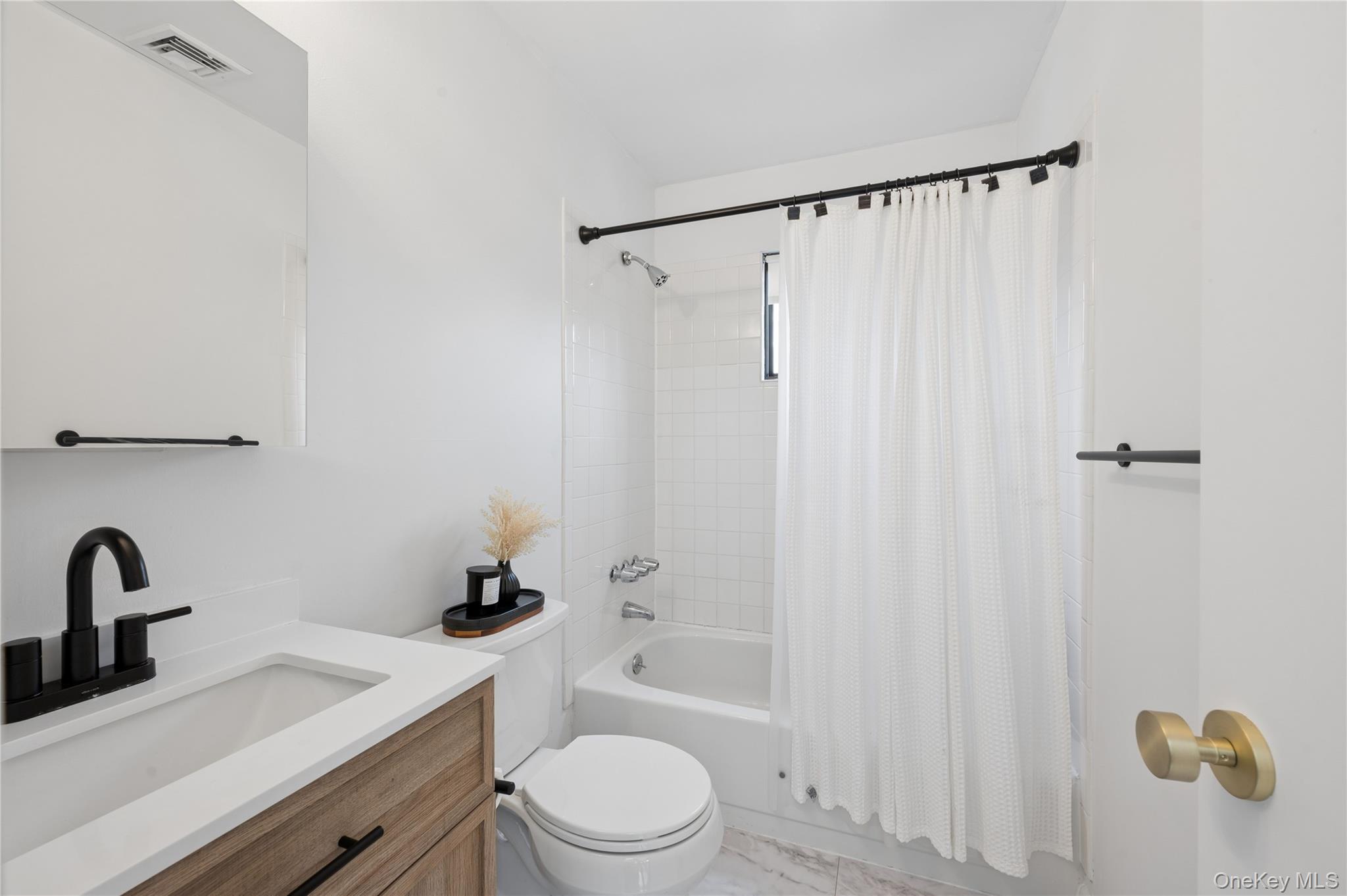 Bright bathroom with a wood-drawer vanity, black fixtures, and a tub-shower with a white curtain.