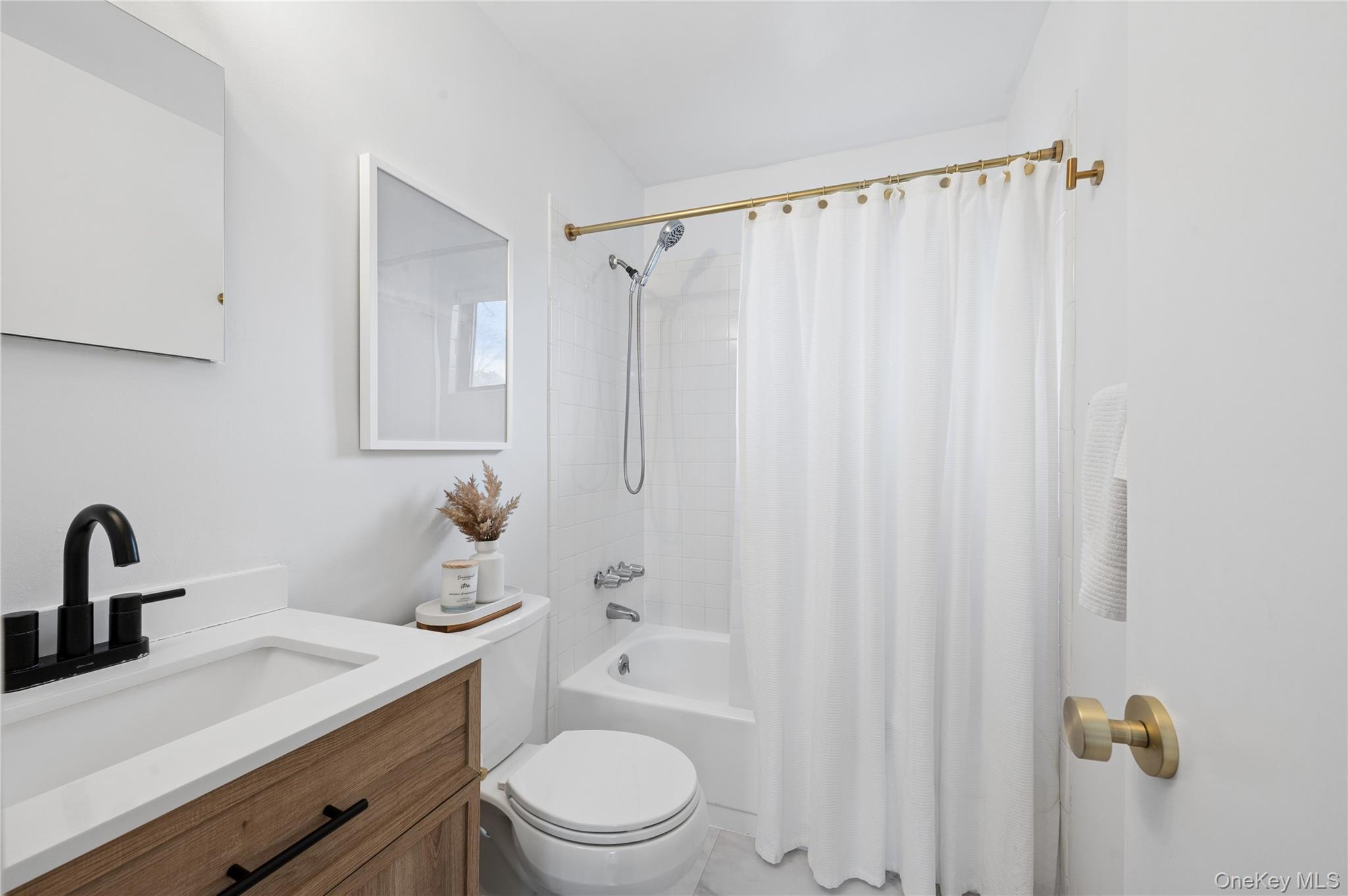 Bright bathroom with a wood vanity, black faucet, and white-curtained tub.