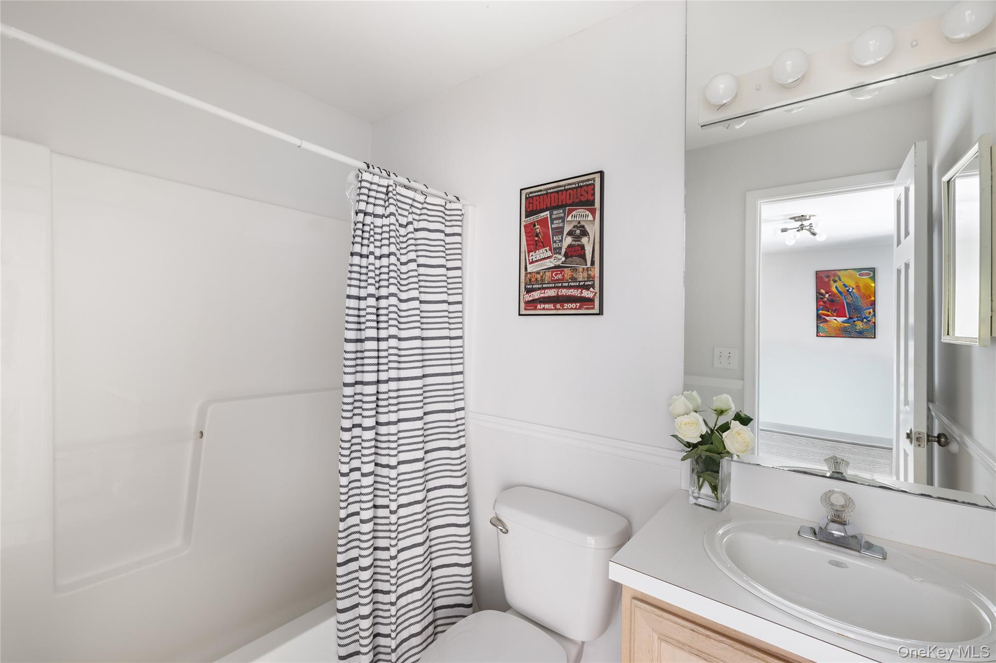 White bathroom with a striped shower curtain, tub, and vanity beneath a mirrored cabinet.