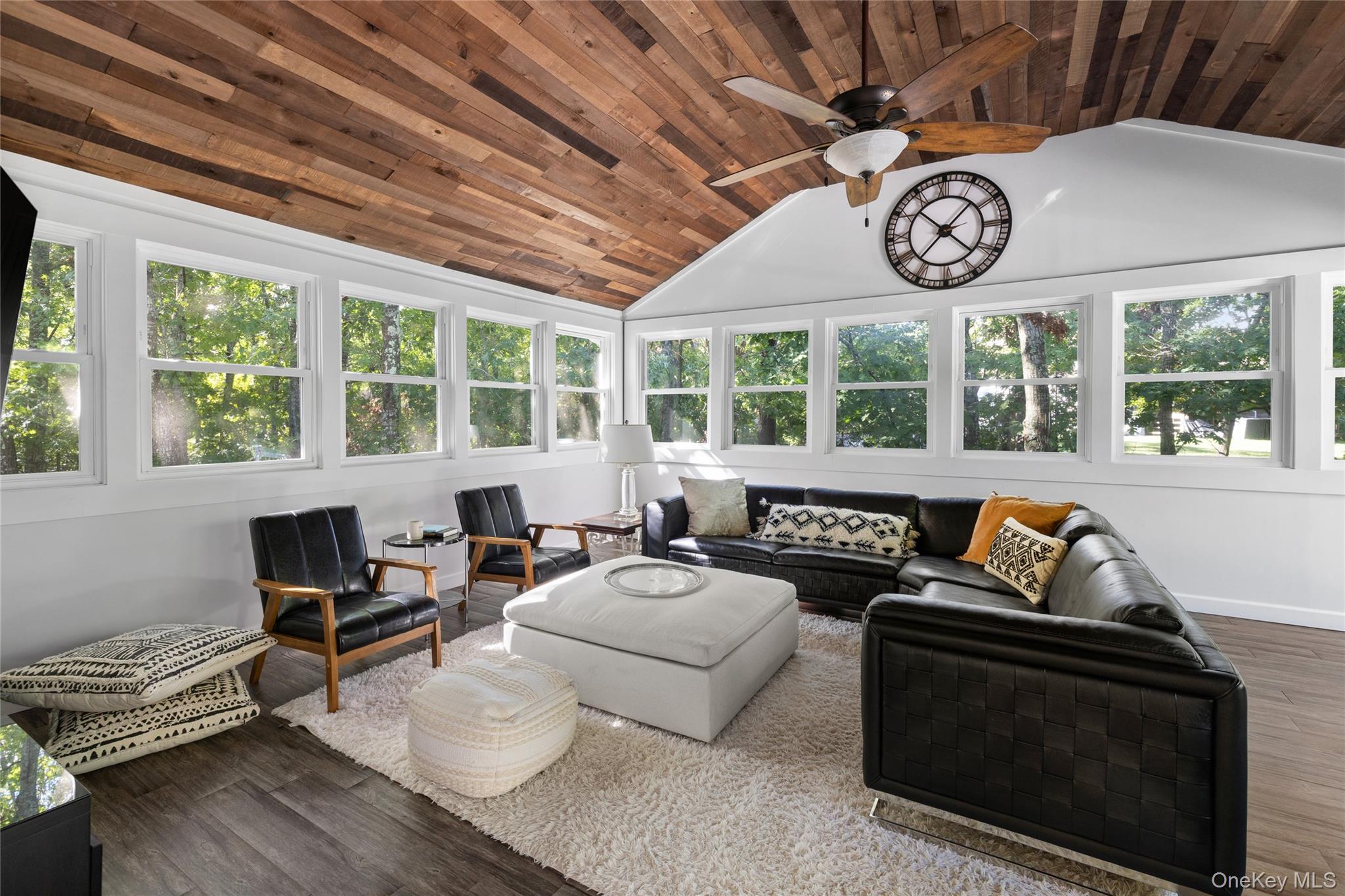 Living room with vaulted wood ceiling, wraparound windows, and black leather sectional.