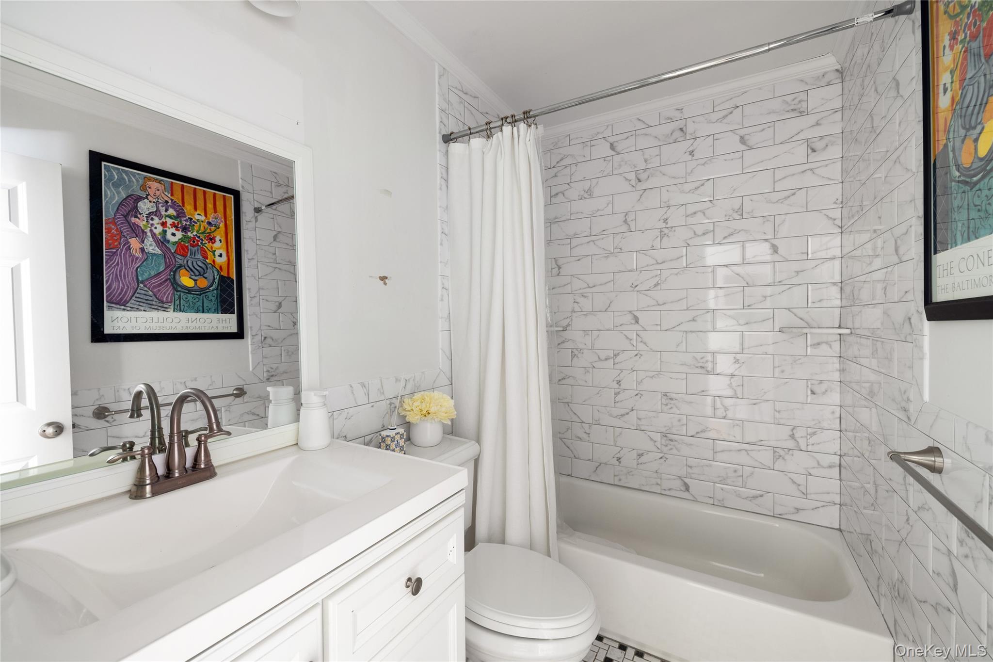 Bathroom with a white vanity, bronze faucets, and a marble-look tiled tub surround.