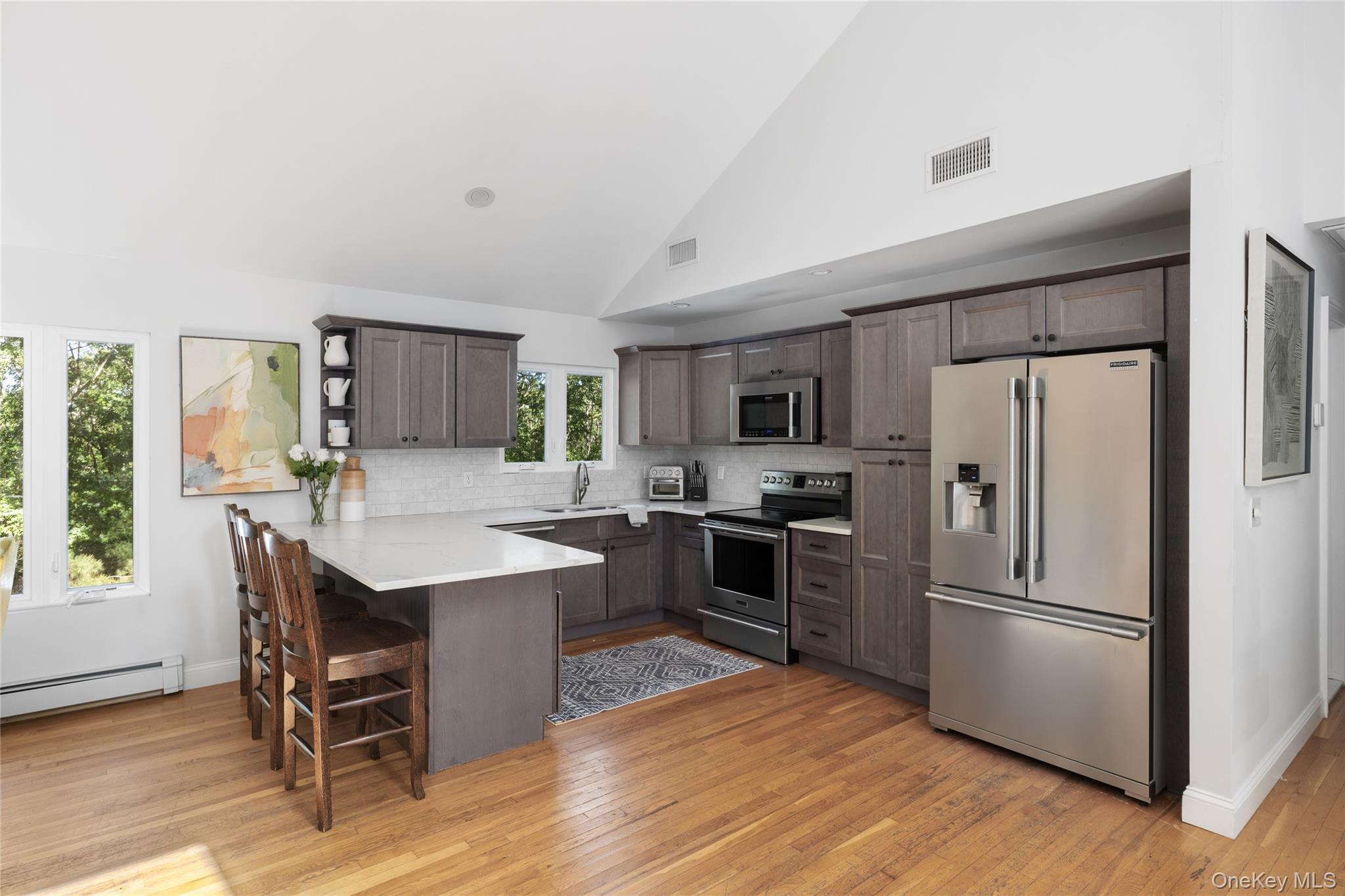 Kitchen with a white seating island, dark cabinets, stainless steel appliances, and vaulted ceiling.
