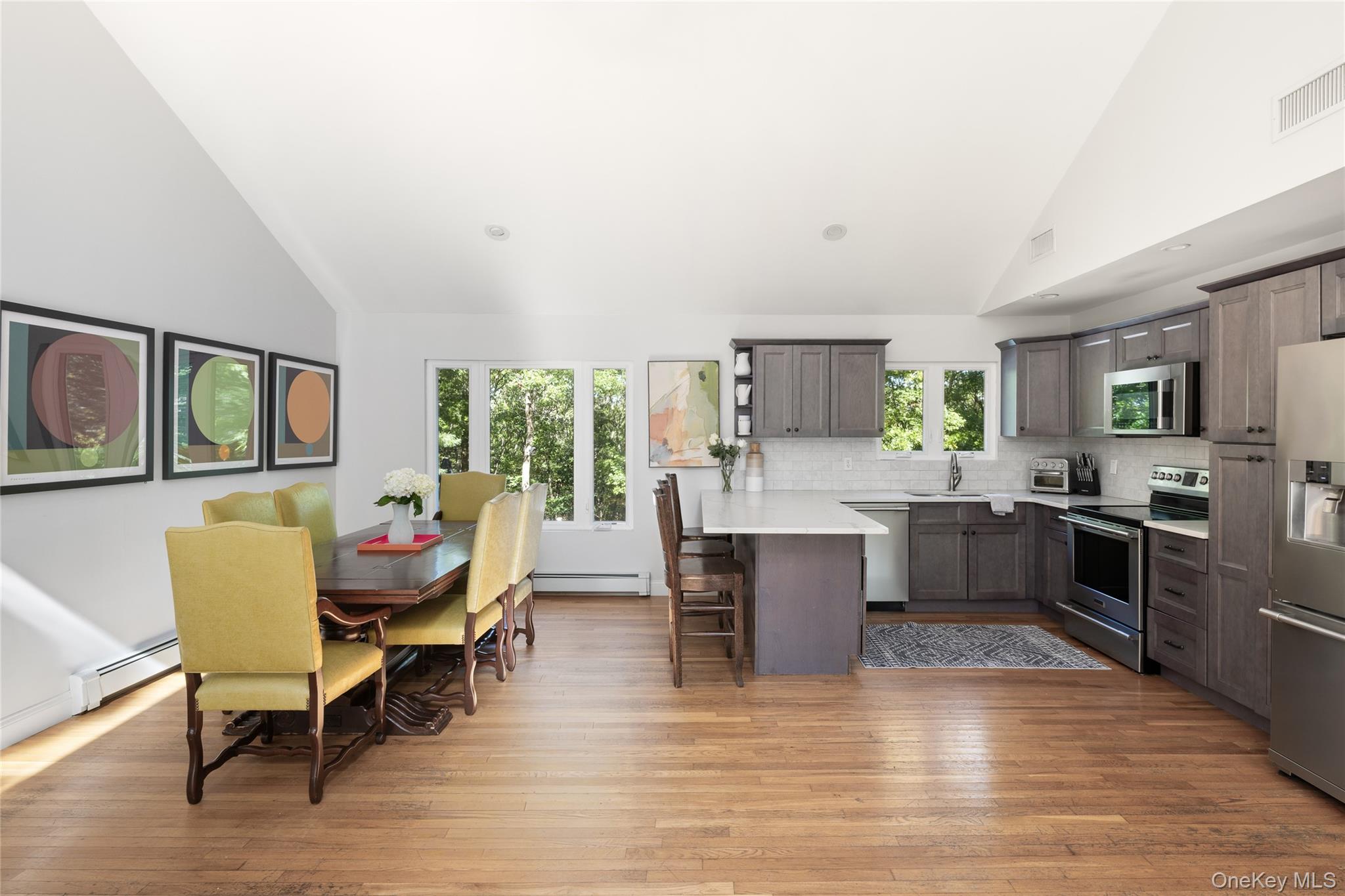 Open kitchen and dining area with gray cabinets, white island, wood floors, and yellow dining chairs.