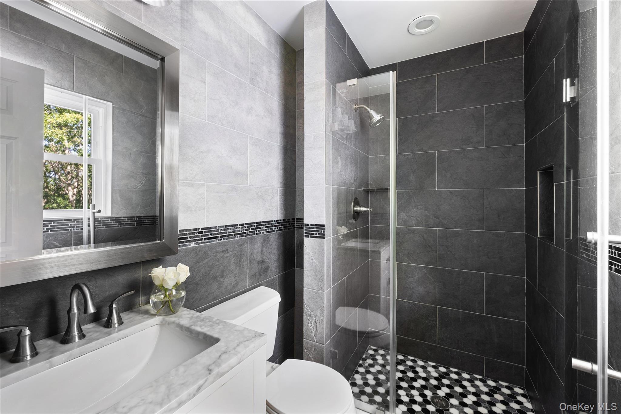 Bathroom with a glass-enclosed tiled shower and white marble vanity.