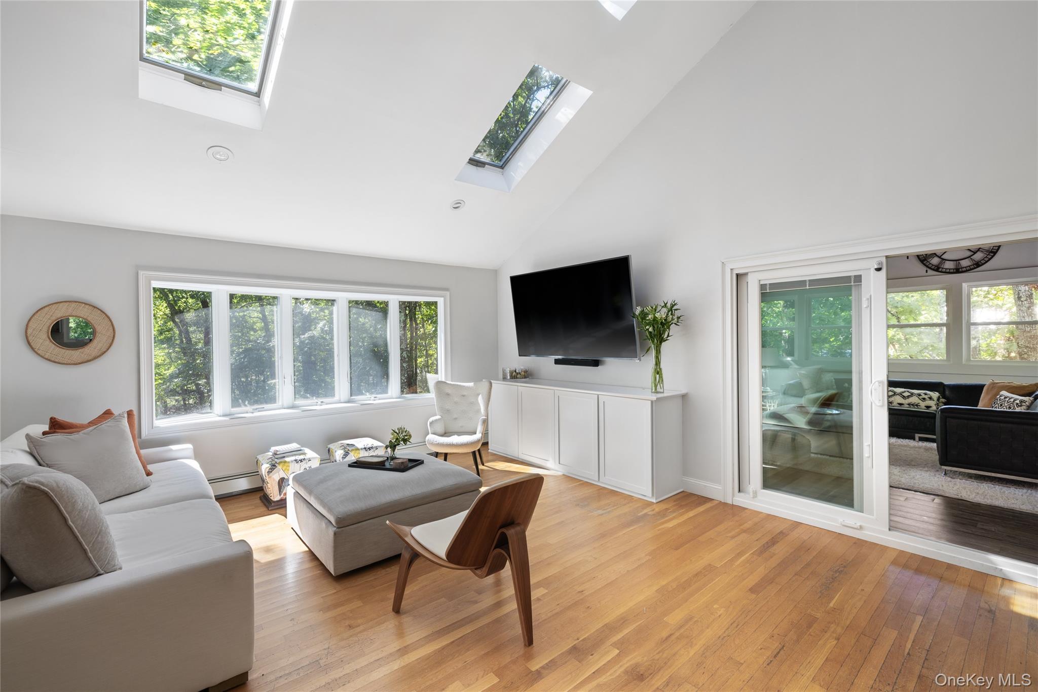 Living room with skylights, hardwood floors, large windows, and a sliding glass door to an adjoining sitting room.