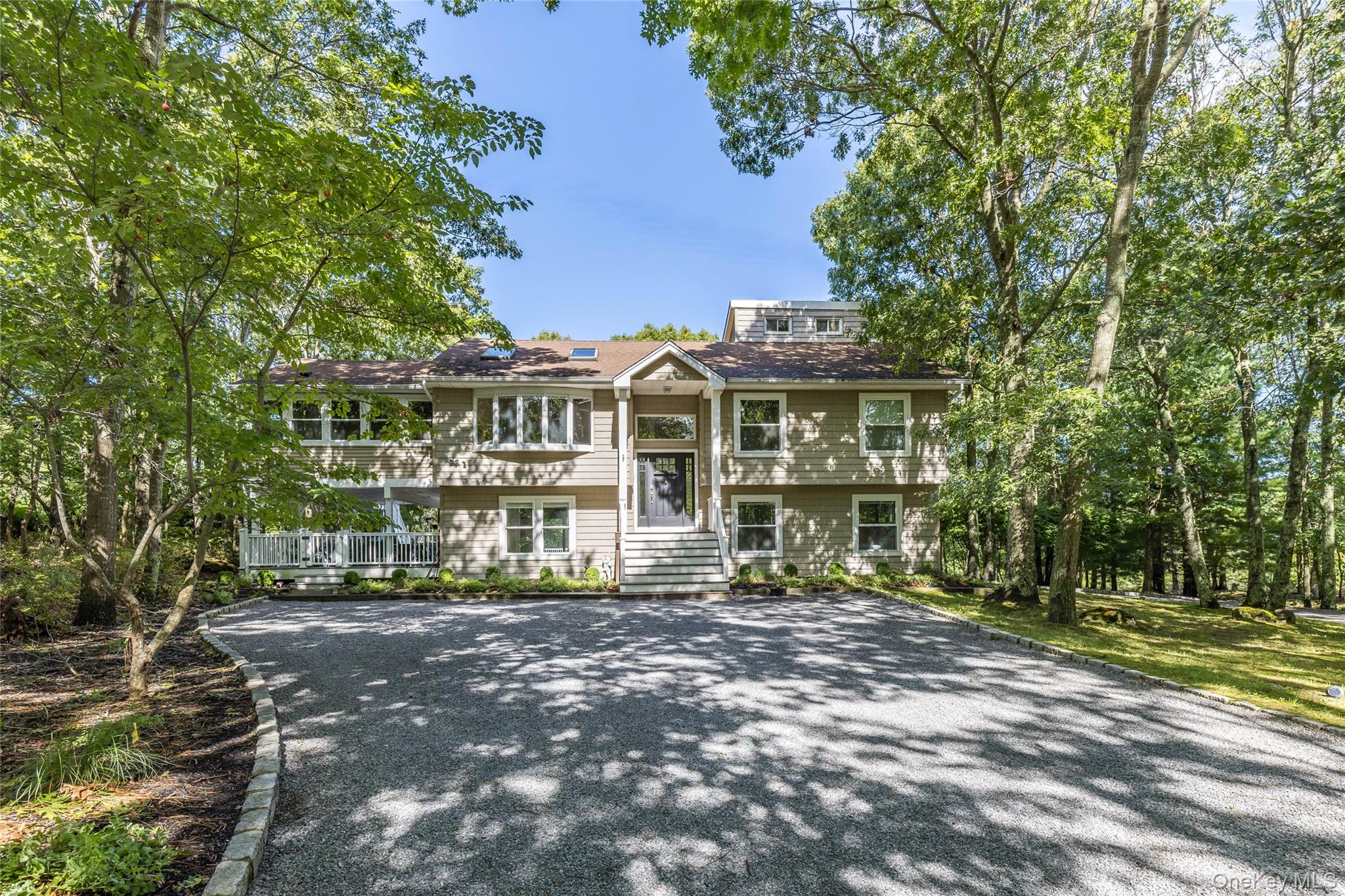 Two-story home with a raised central entry and broad gravel driveway beneath mature trees.