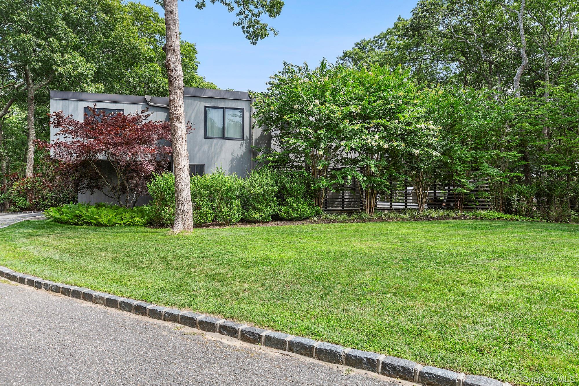 Modern gray house nestled among mature trees, with a broad green lawn.