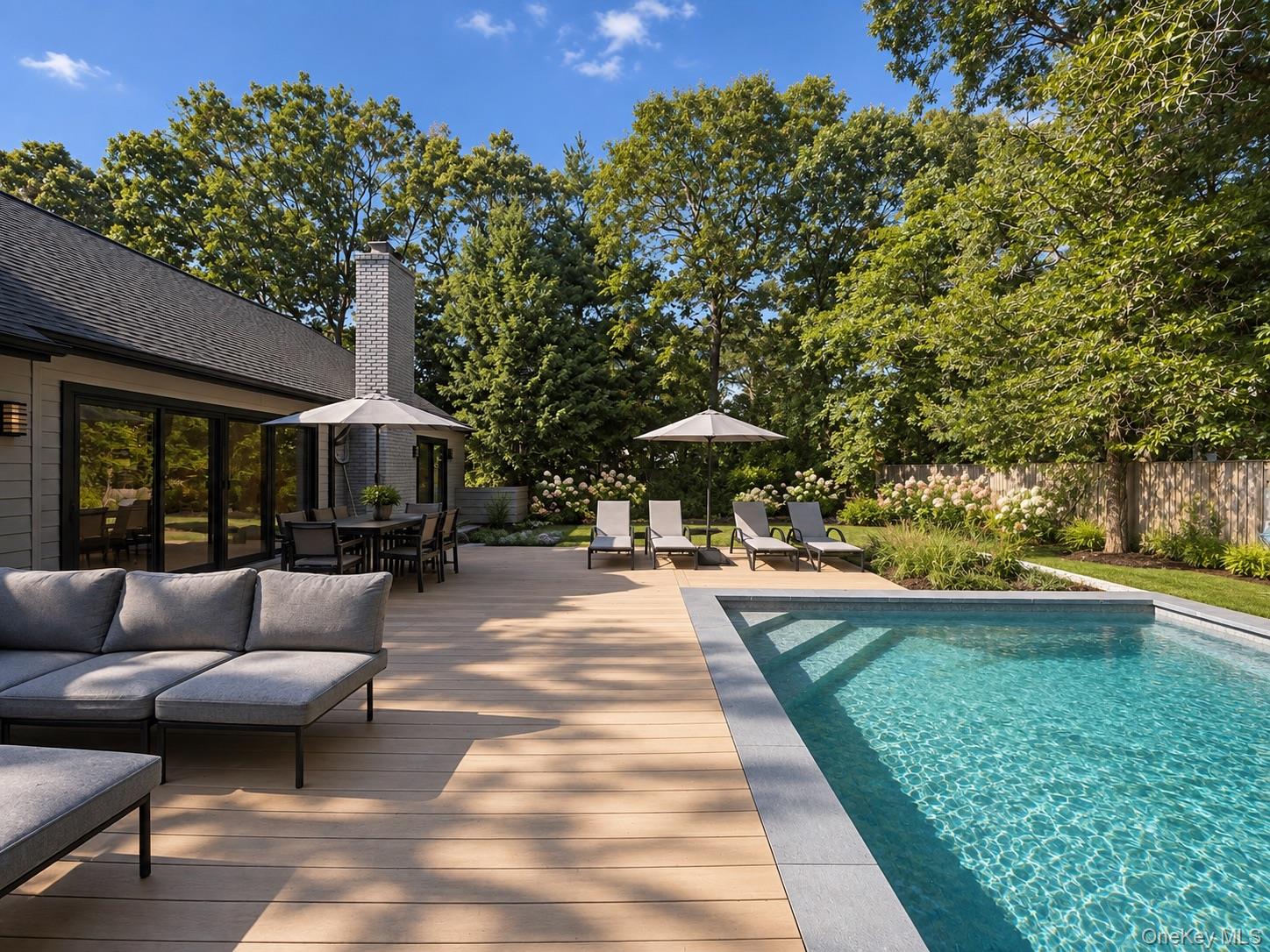 Backyard pool beside a wood deck with lounge seating, dining area, and mature trees.