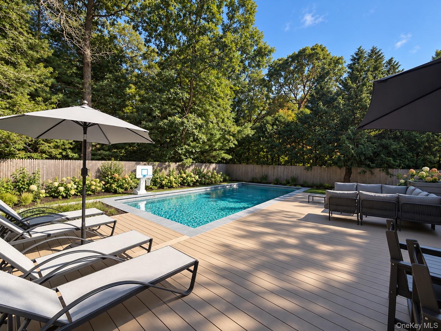 Backyard pool and wood deck with lounge chairs, outdoor seating, and mature trees.