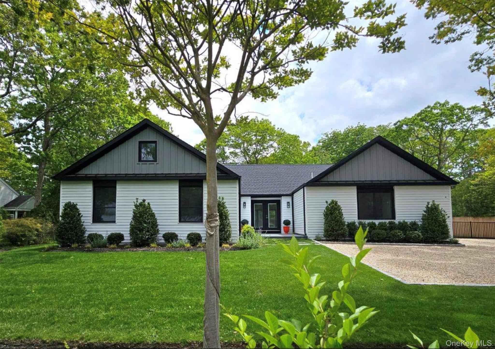White single-story house with twin dark-trimmed gables, a landscaped lawn, and gravel driveway.