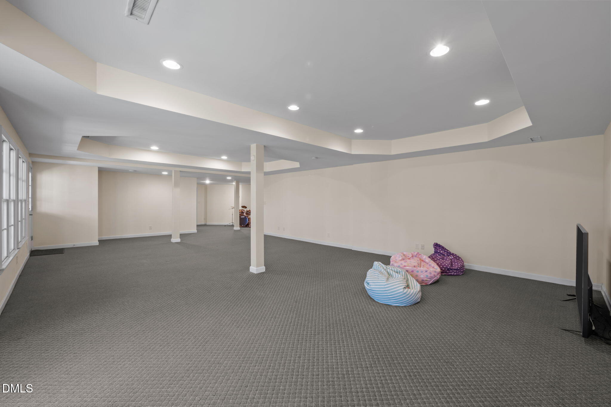Finished basement recreation room with gray carpet, beanbag chairs, and a drum set.