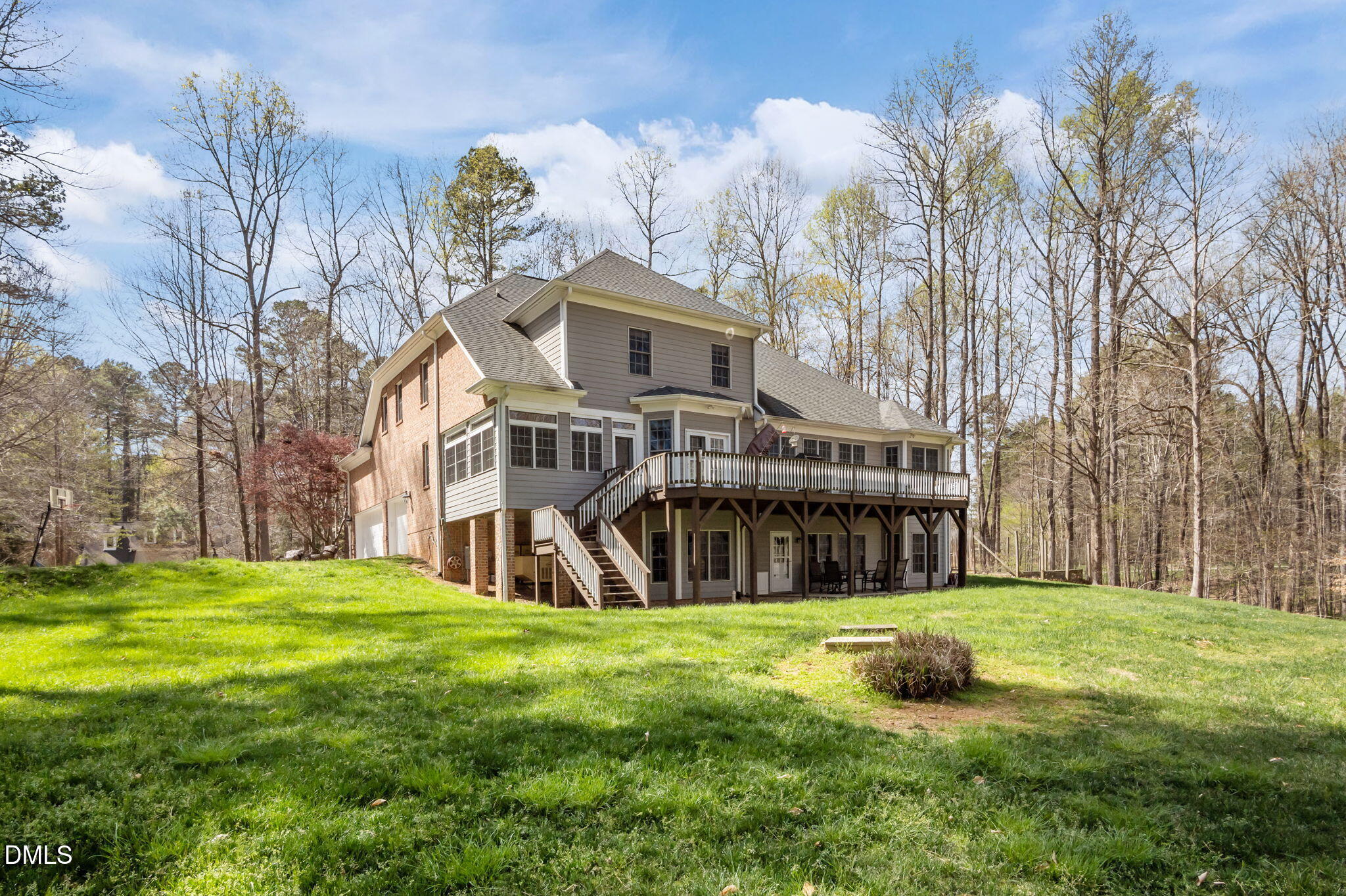Rear of a two-story brick and gray-sided house with a raised deck overlooking a grassy, wooded yard.