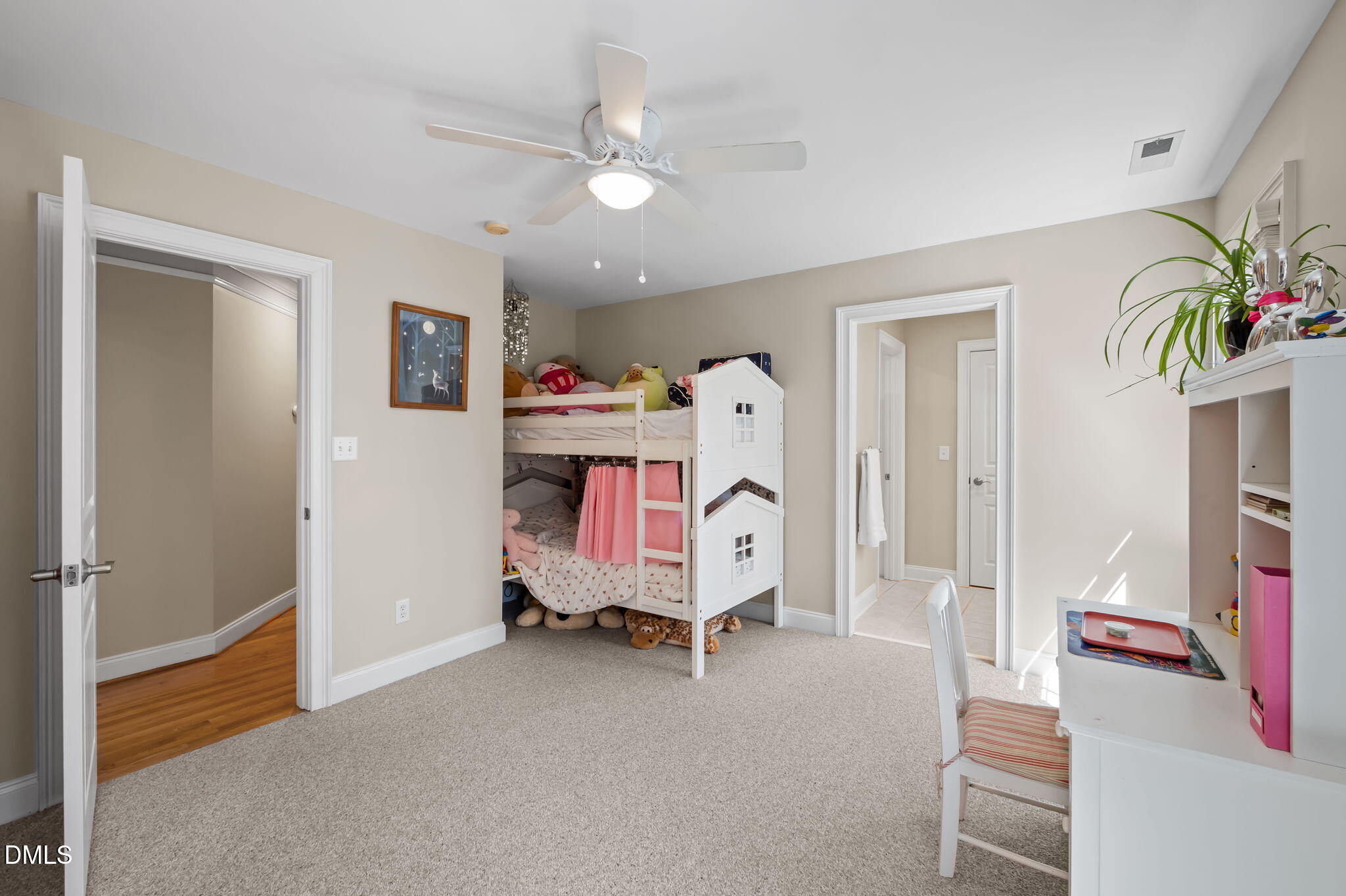 Children’s bedroom with a white house-shaped bunk bed, stuffed animals, and a white desk.