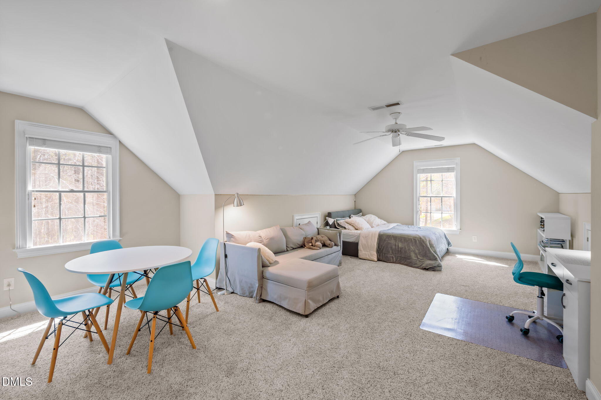 Furnished upstairs bedroom with a sloped ceiling, bed, sofa, and blue dining chairs.