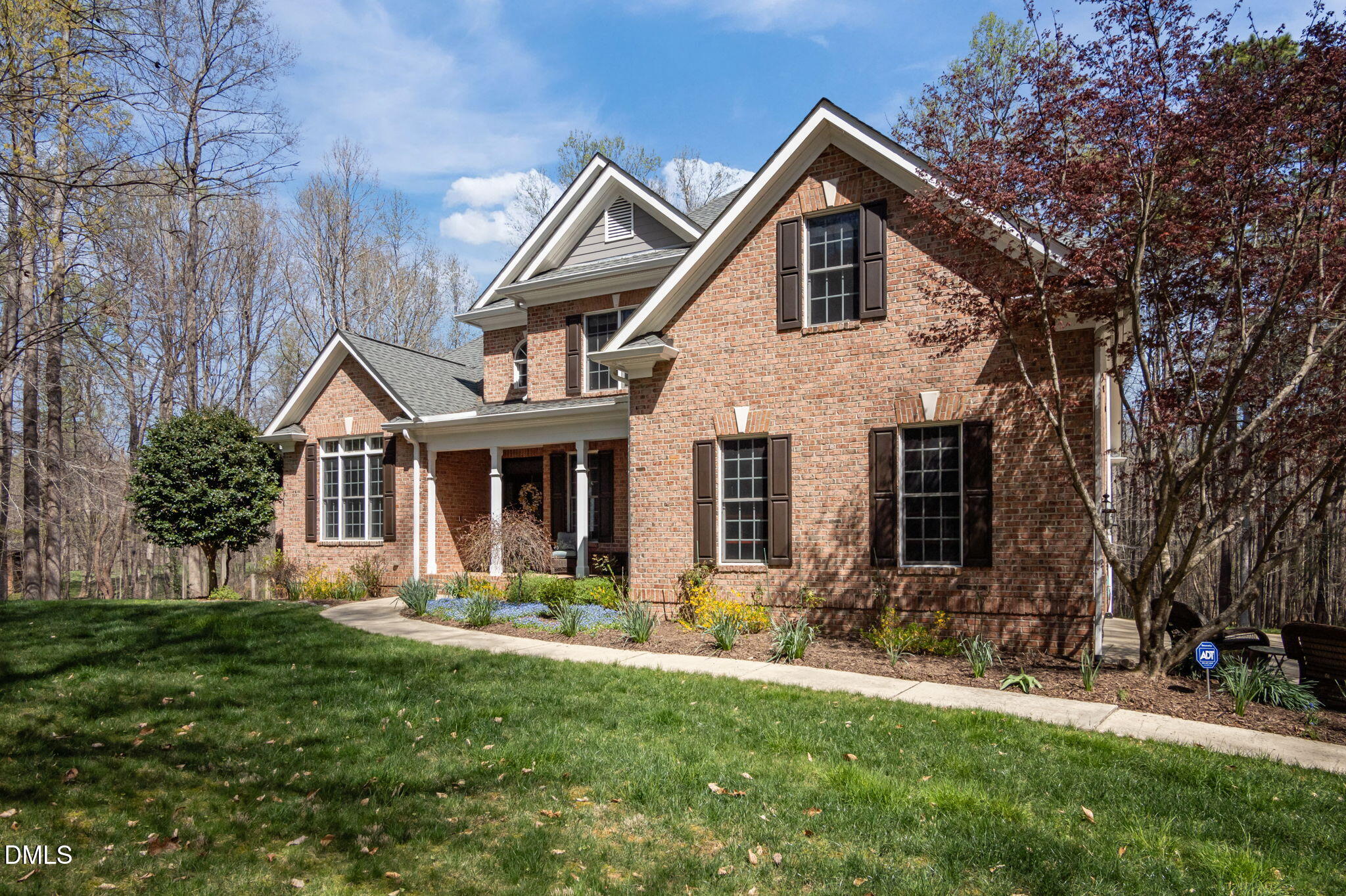 Red-brick two-story house with gabled roofs, covered porch, landscaped garden, and curved walkway.