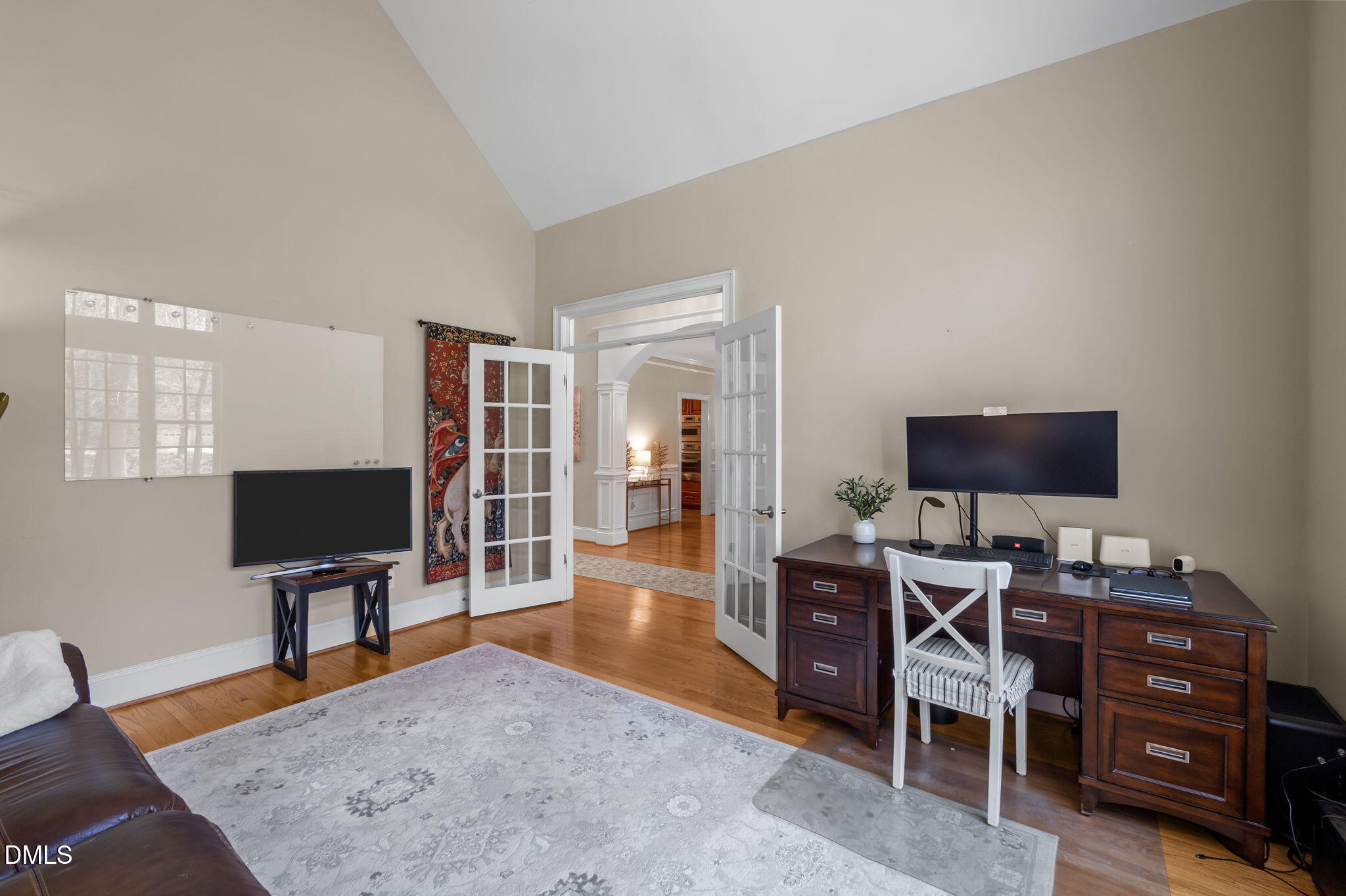 Furnished home office with vaulted ceiling, French doors, hardwood floors, and a large dark wood desk.