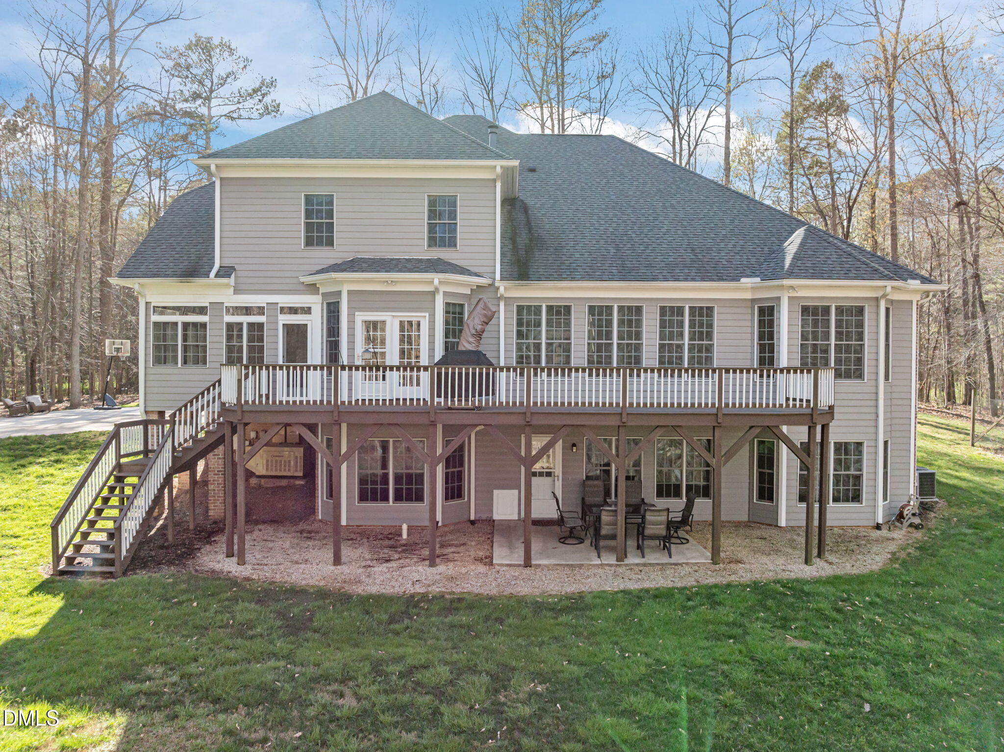 Rear of a two-story gray home with a raised deck and stairs overlooking a wooded yard.