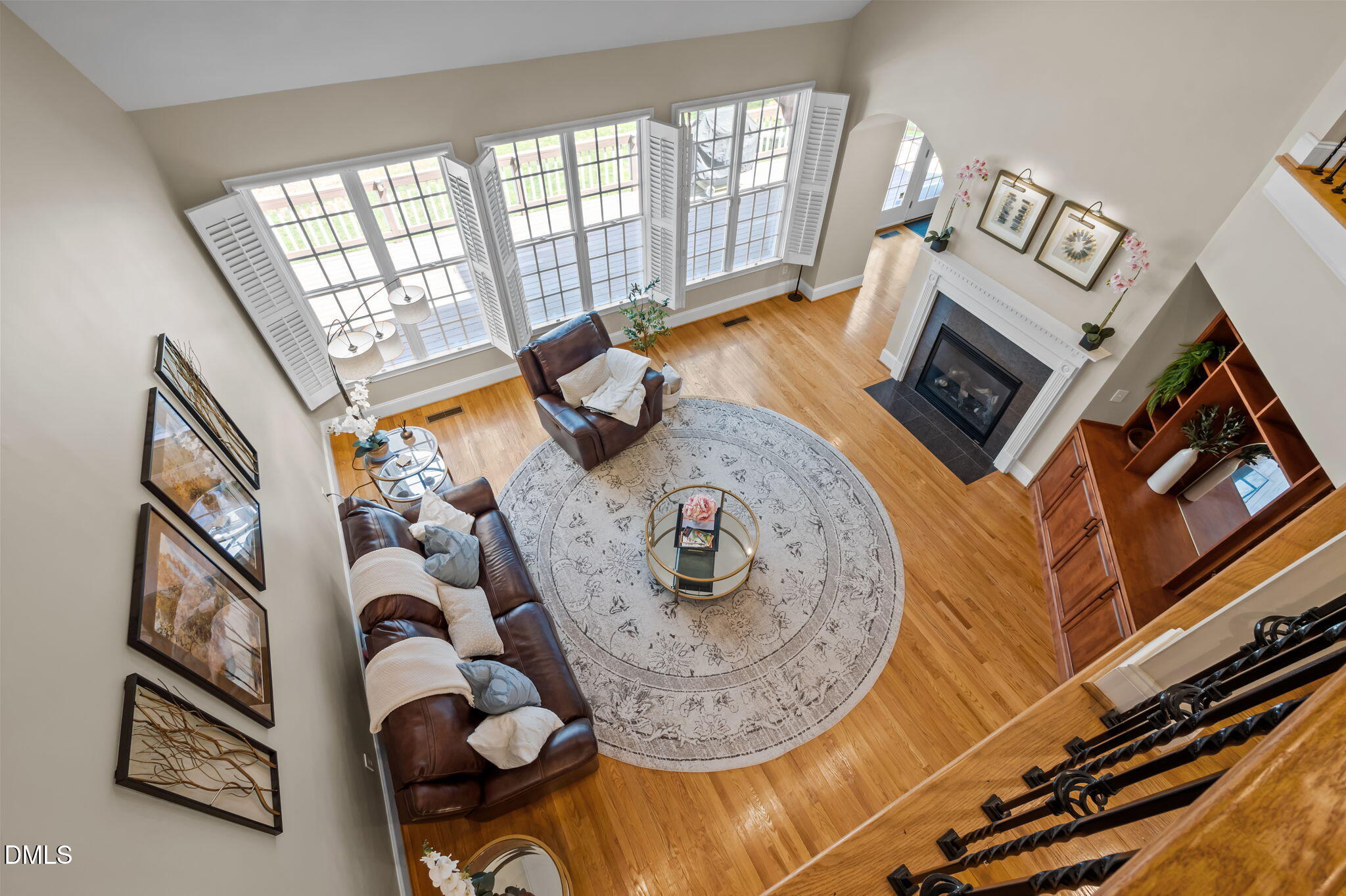 Furnished living room with tall shuttered windows, leather seating, hardwood floors, and a fireplace.