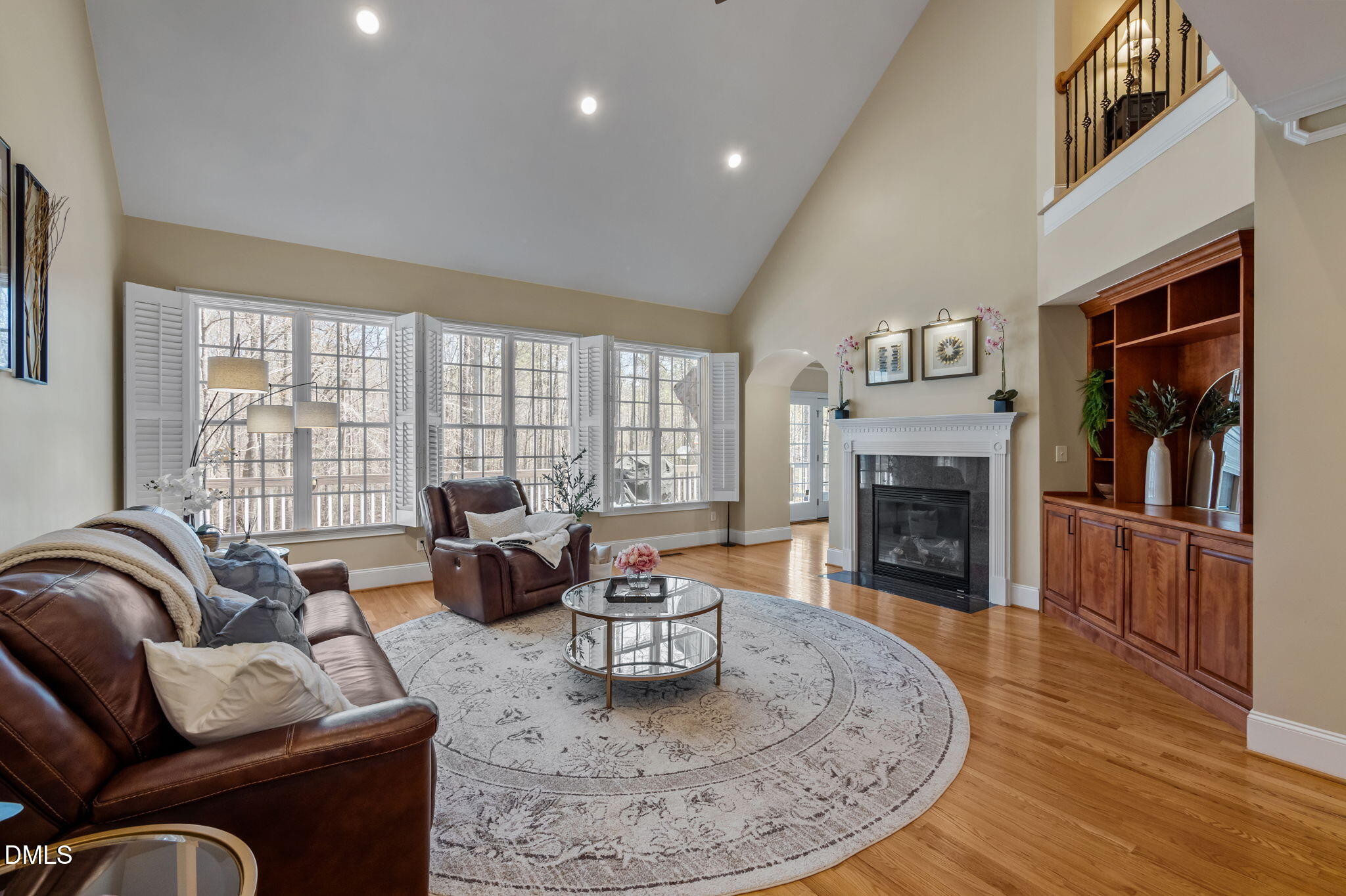 Living room with vaulted ceiling, leather seating, white fireplace, and large shuttered windows.