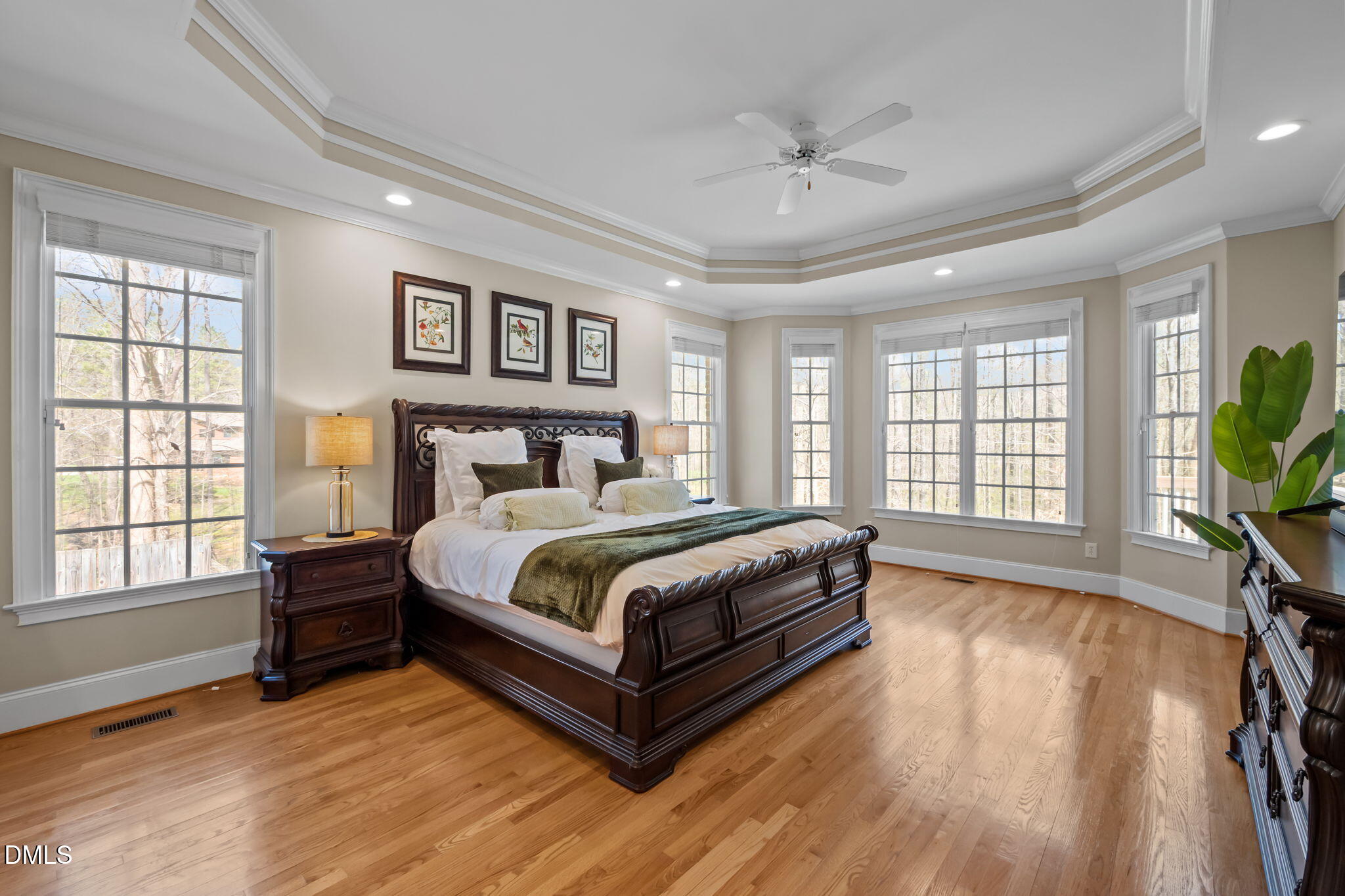 Primary bedroom with a carved dark wood bed, hardwood floors, and large windows.