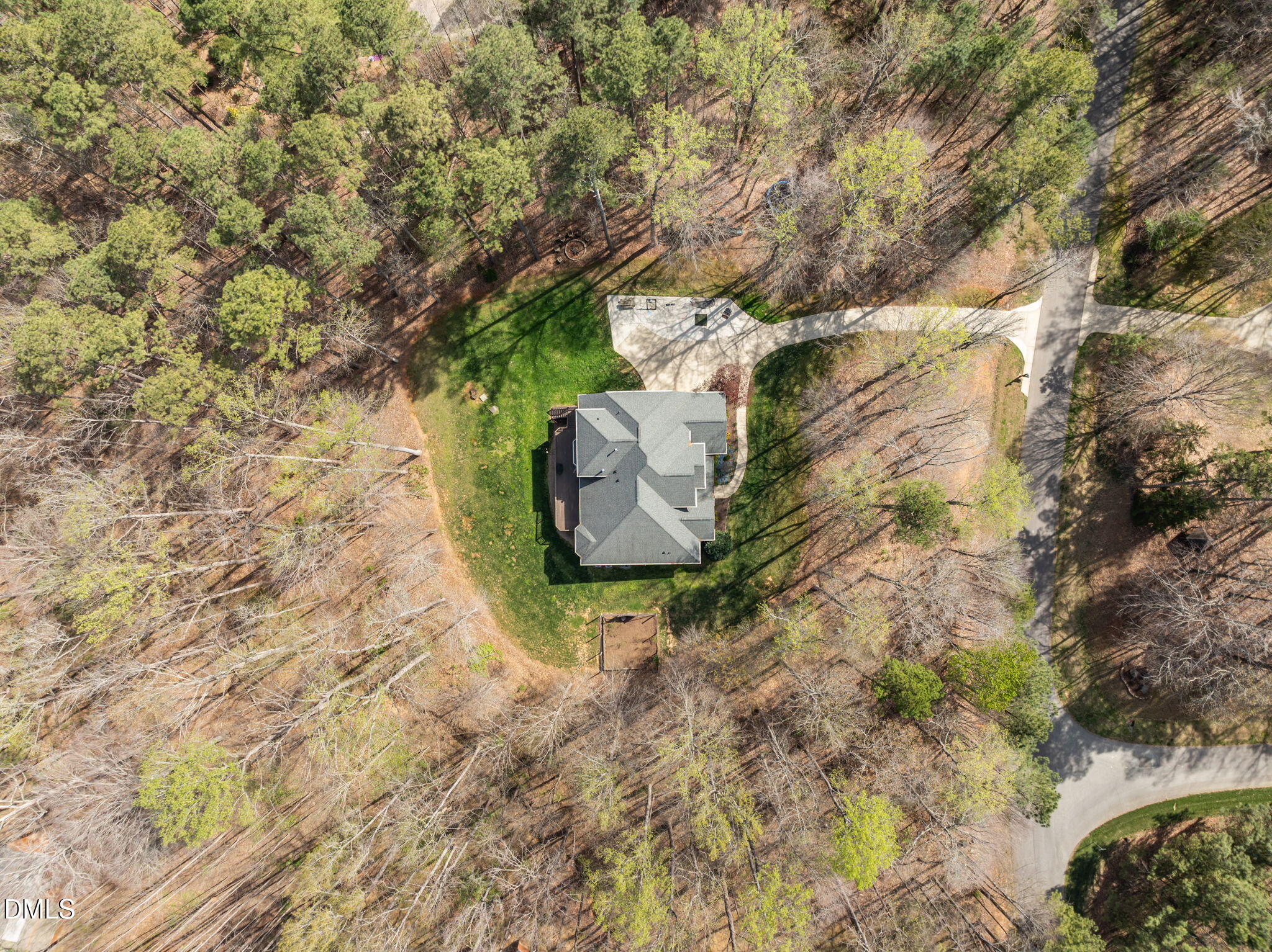 Aerial view of a house surrounded by trees, with a green lawn and winding driveway.
