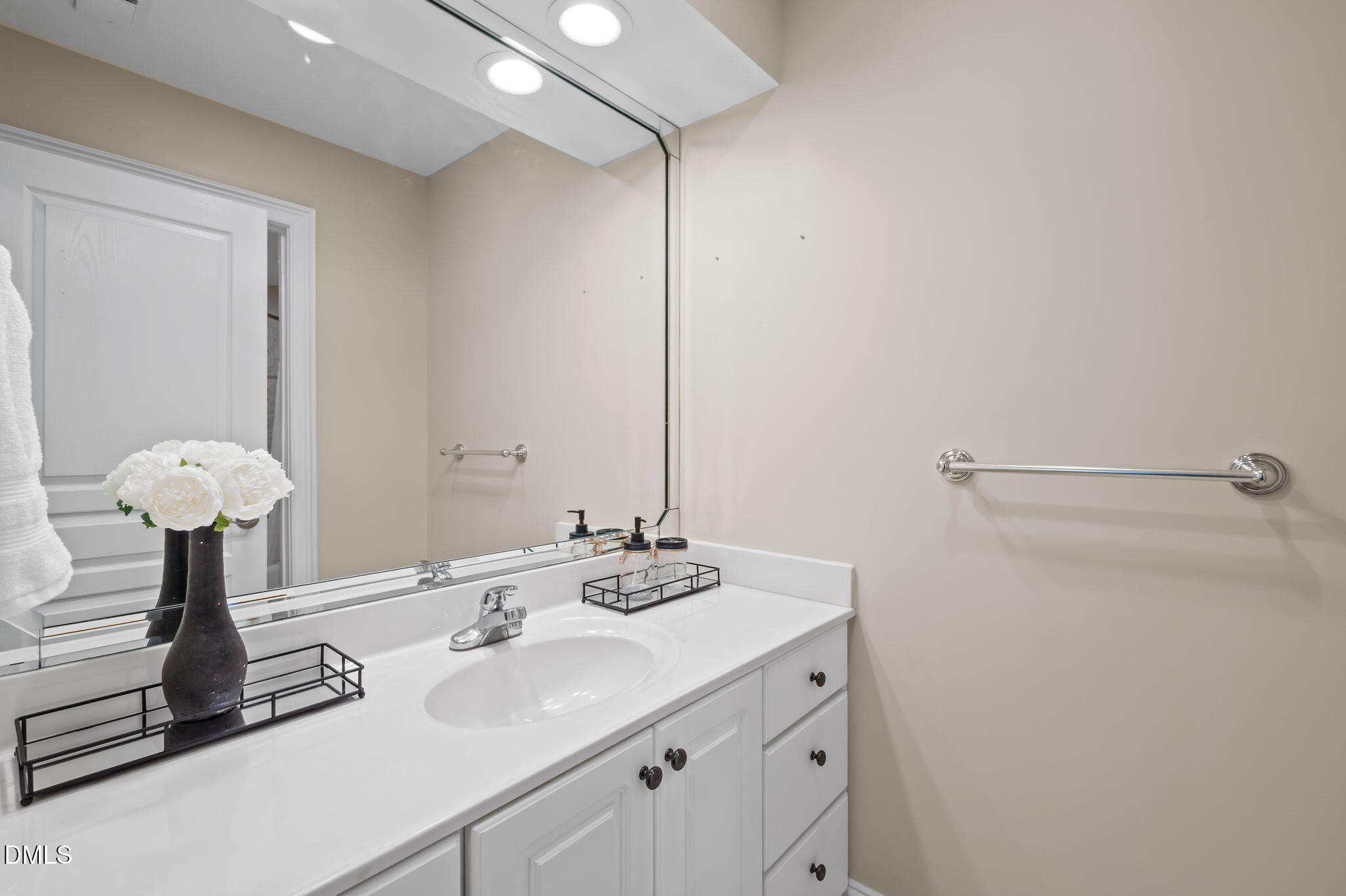 Bathroom vanity with a white sink, large mirror, chrome towel bar, and flowers on the counter.