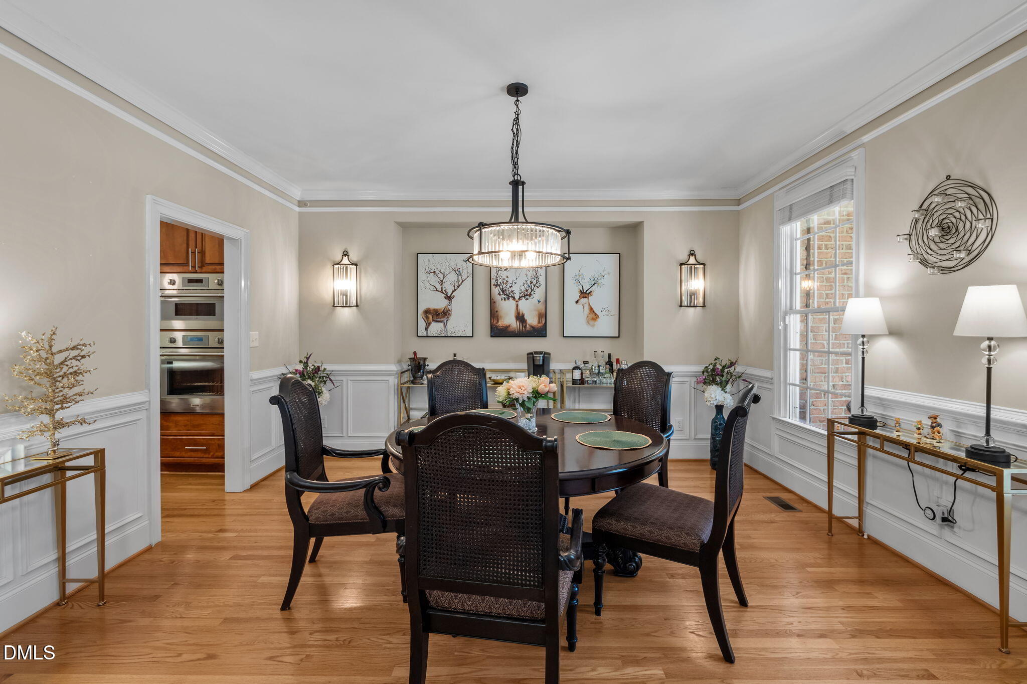 Dining room with a dark wood table, woven-back chairs, crystal chandelier, and white wainscoting.
