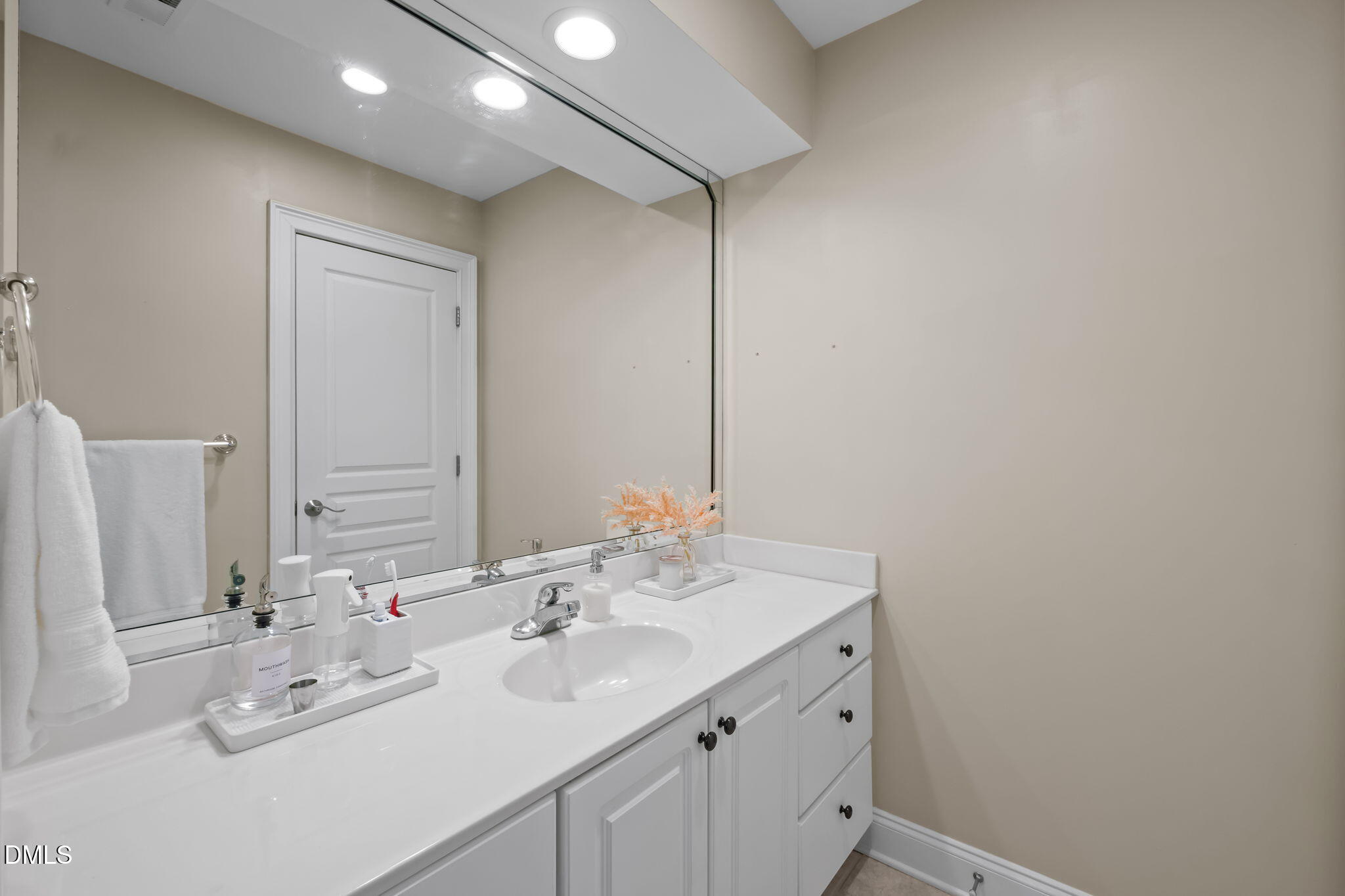 Bathroom vanity with a long white counter, oval sink, paneled cabinetry, and large mirror.
