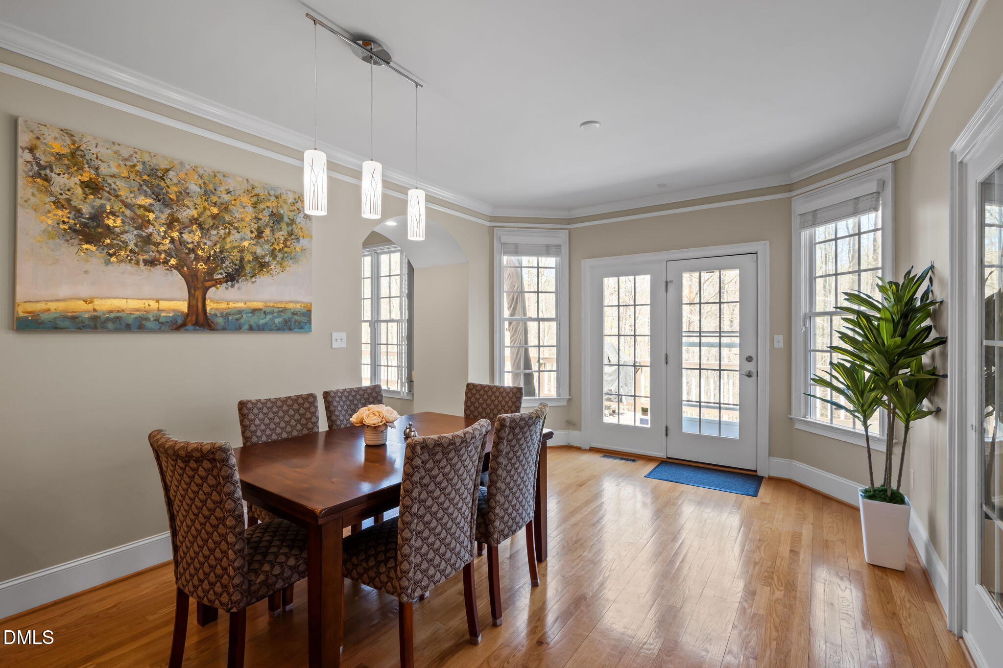 Dining room with a dark wood table, patterned chairs, and French doors overlooking trees.