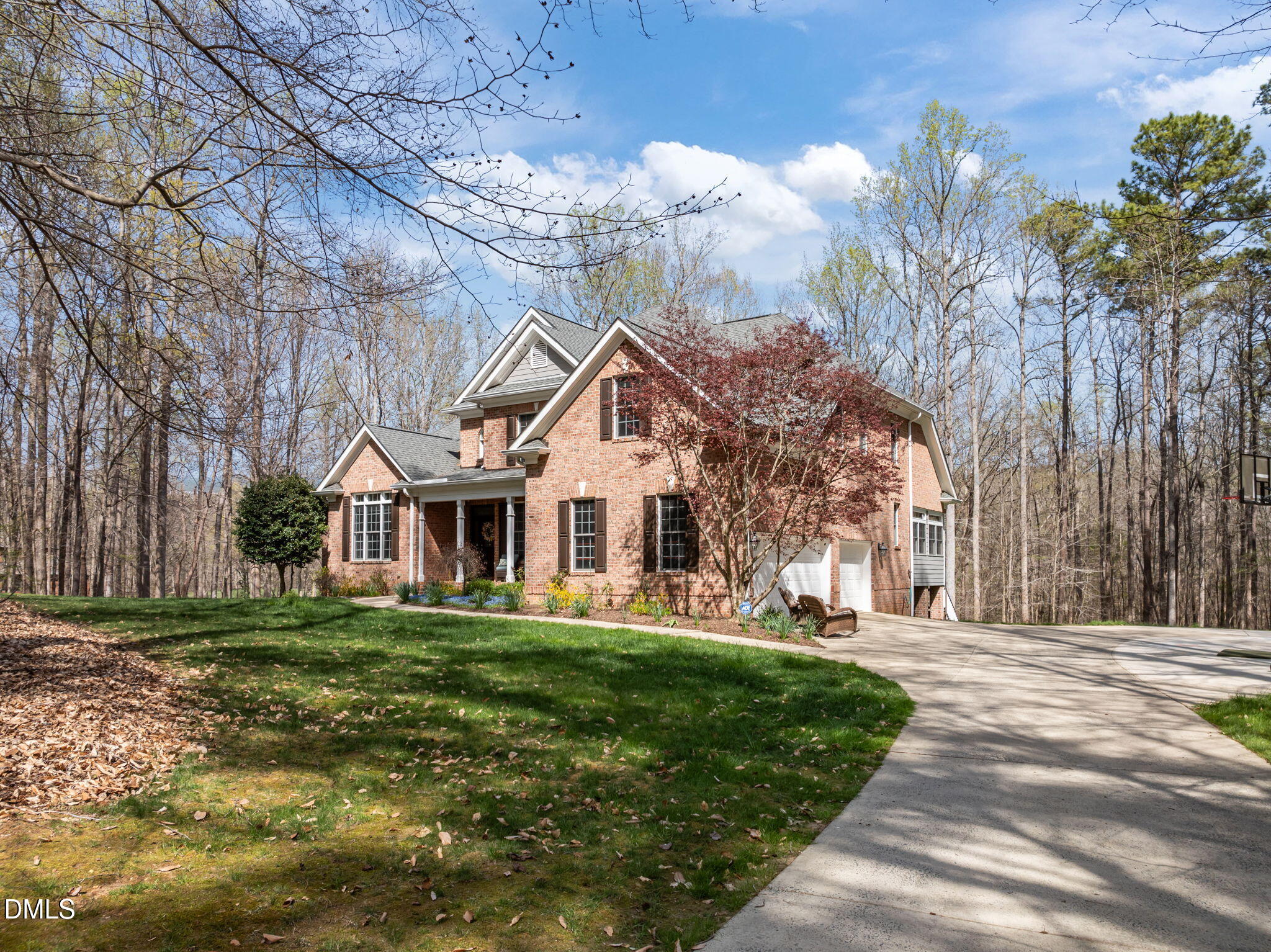 Two-story brick home with a covered porch, attached garage, and wooded surroundings.