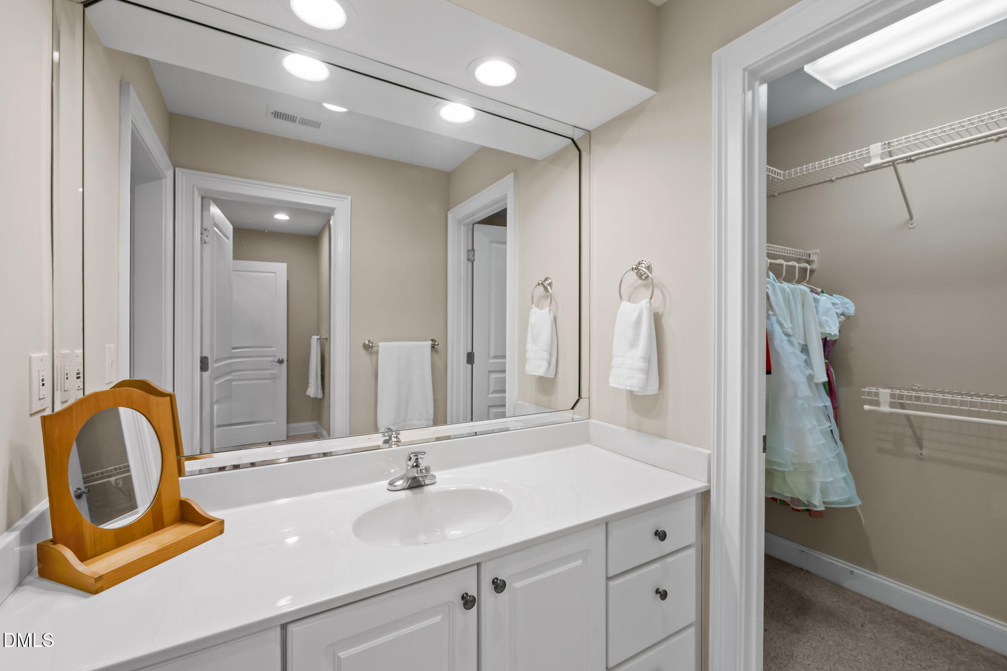 Bathroom with a white vanity and large mirror beside an open walk-in closet.