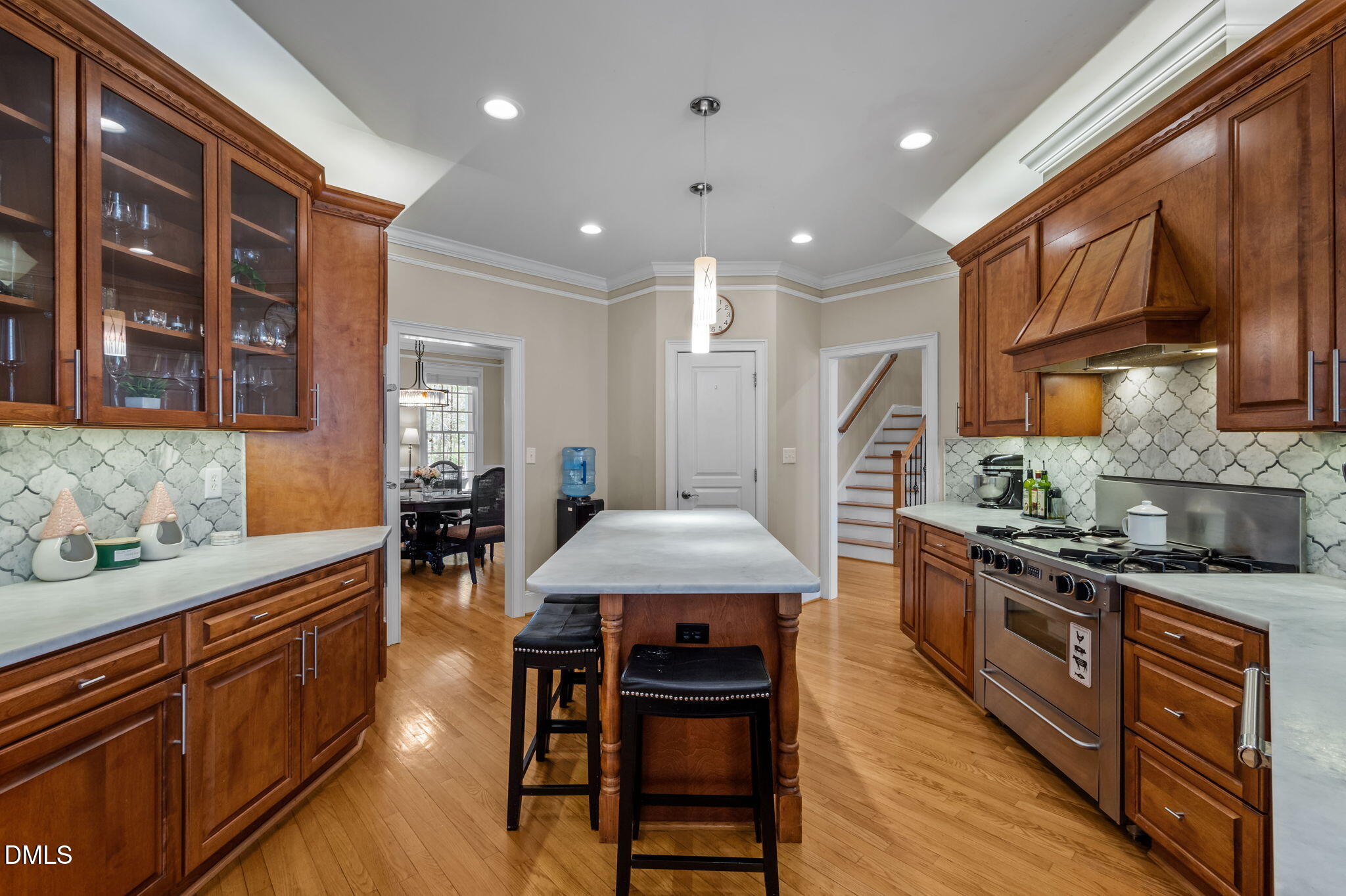 Kitchen with rich wood cabinetry, patterned tile backsplash, and a large island with stools.