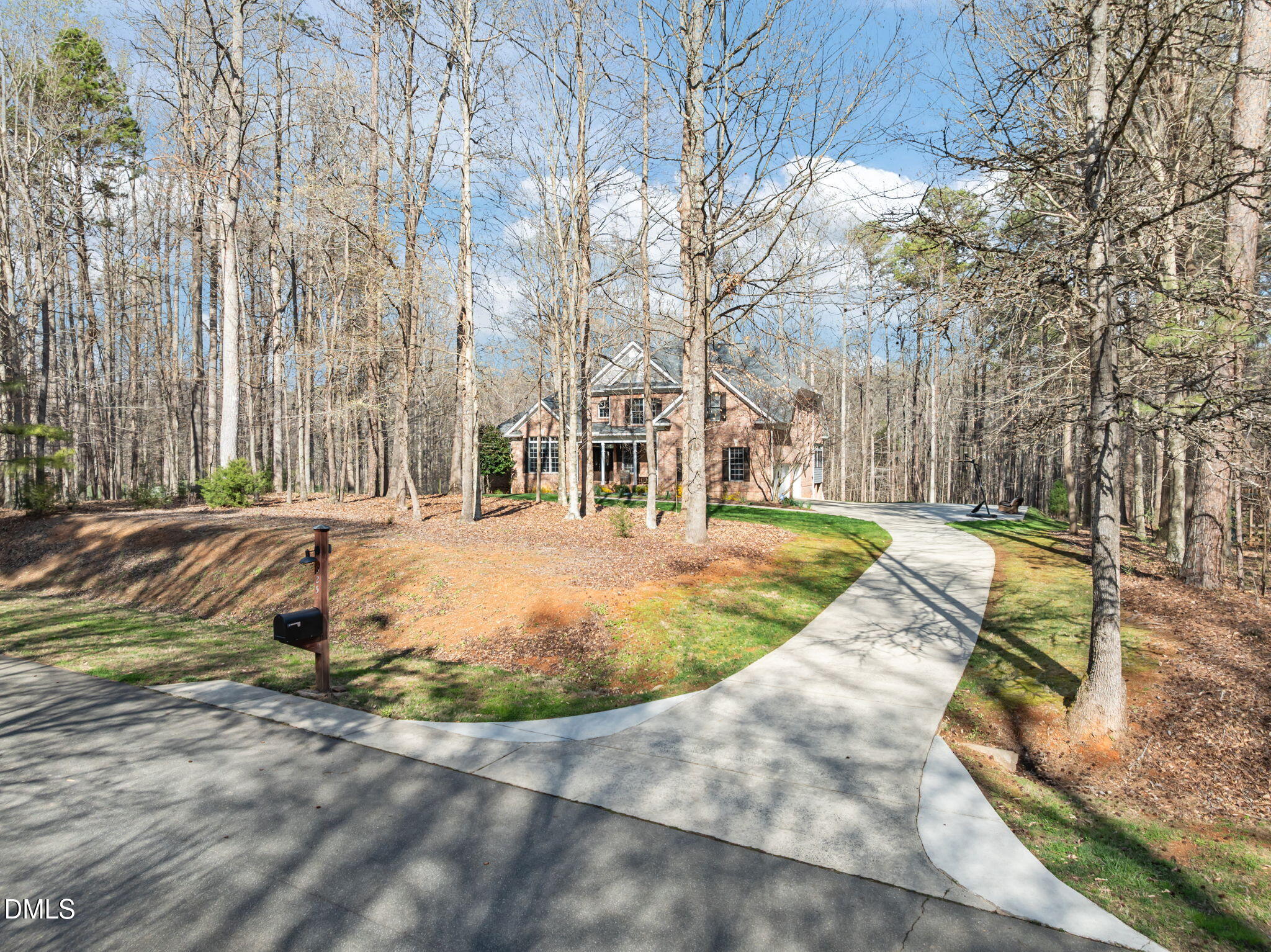 Brick house among leafless trees, with a curved concrete driveway and roadside mailbox.