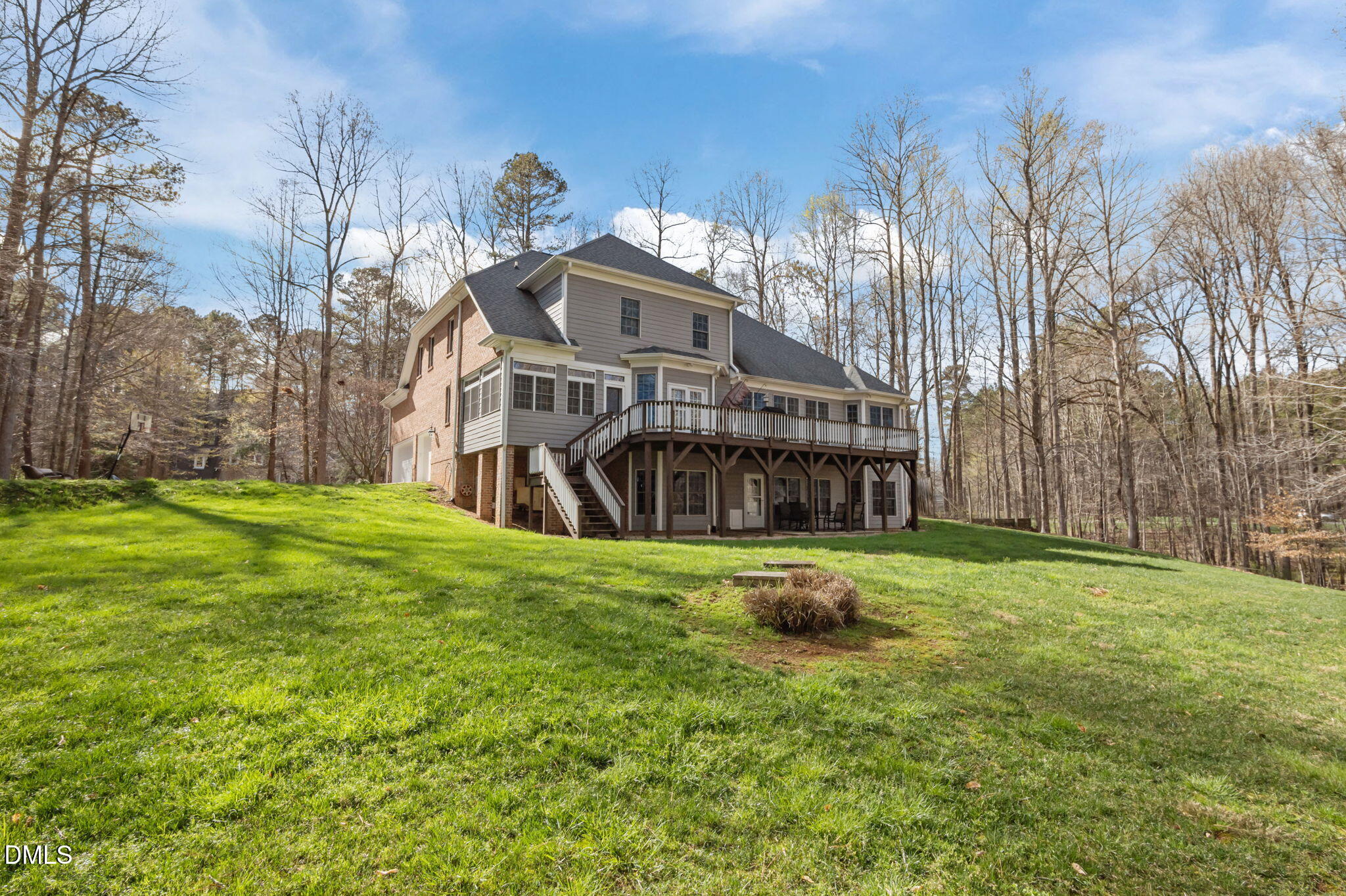 Rear of a two-story home with a raised deck and covered patio, surrounded by woods.
