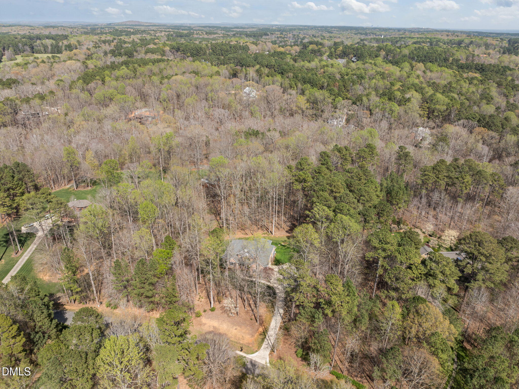 Aerial view of a house and curved driveway nestled among extensive woods.