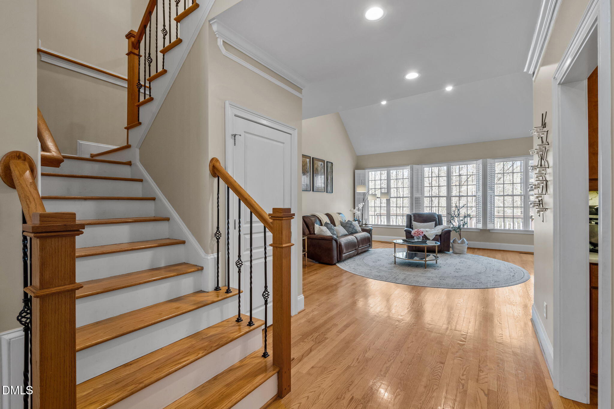 Living room and staircase with hardwood floors, dark iron balusters, and a wall of shuttered windows.