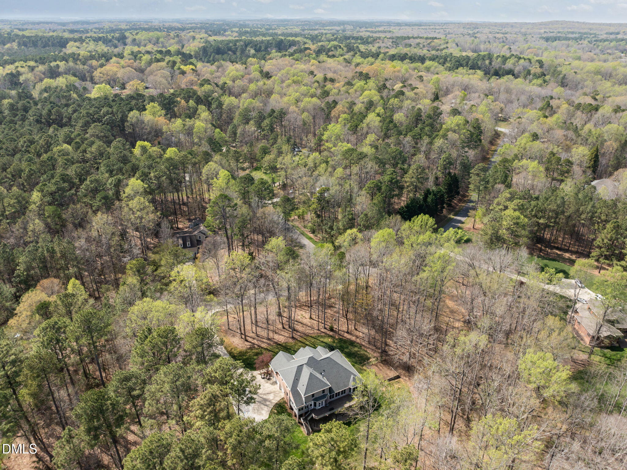 Aerial view of a large house nestled among dense trees, with a driveway and winding road nearby.