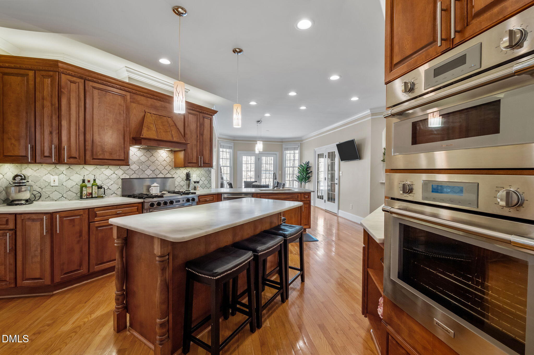 Kitchen with a large island, rich wood cabinetry, patterned tile backsplash, and stainless steel double ovens.