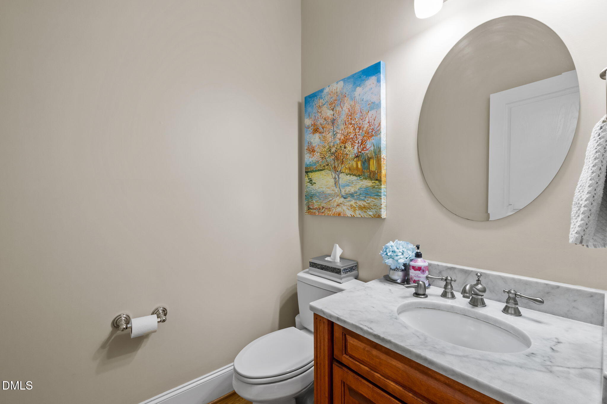 Bathroom with a wood vanity, marble countertop, oval mirror, and colorful tree painting.
